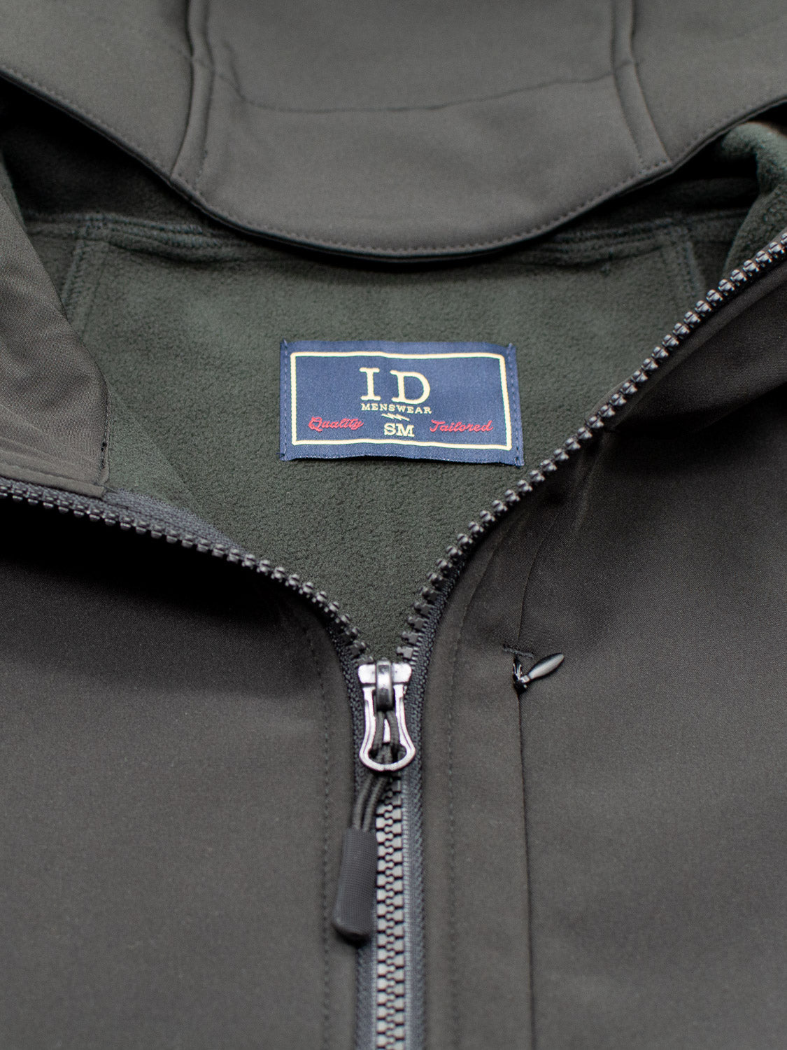 Close-up of a dark green Fairbanks Soft Shell Hooded Jacket by ID Menswear, featuring a visible zipper thats partially open to reveal the inner fleece lining. The lightweight jacket also includes an additional chest pocket for convenience.