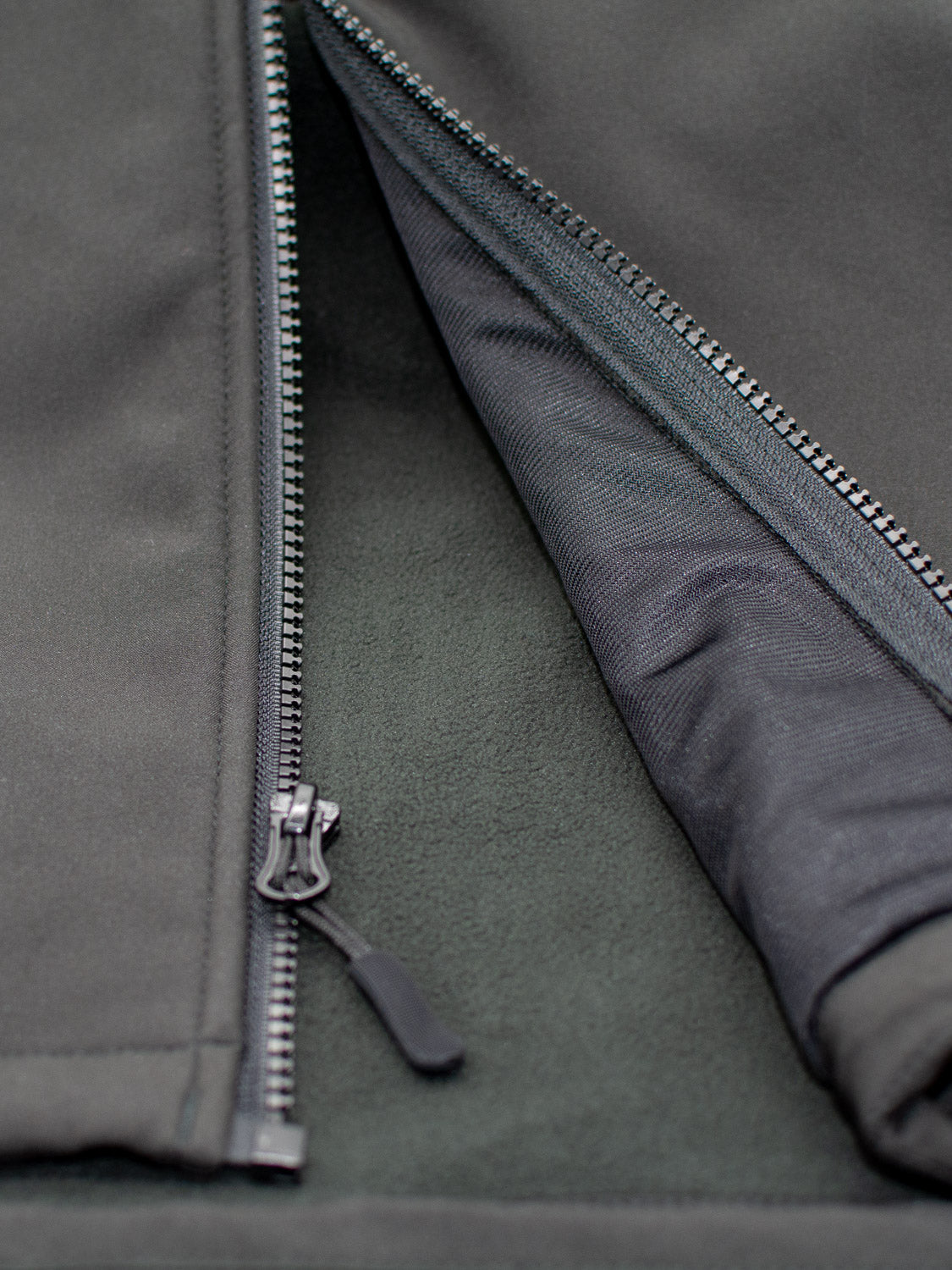 A close-up of the Fairbanks Soft Shell Hooded Jacket by ID Menswear shows a partially unzipped view, revealing the metal zipper and interior lining. The fabric is a comfortable polyester blend with both soft and textured elements.