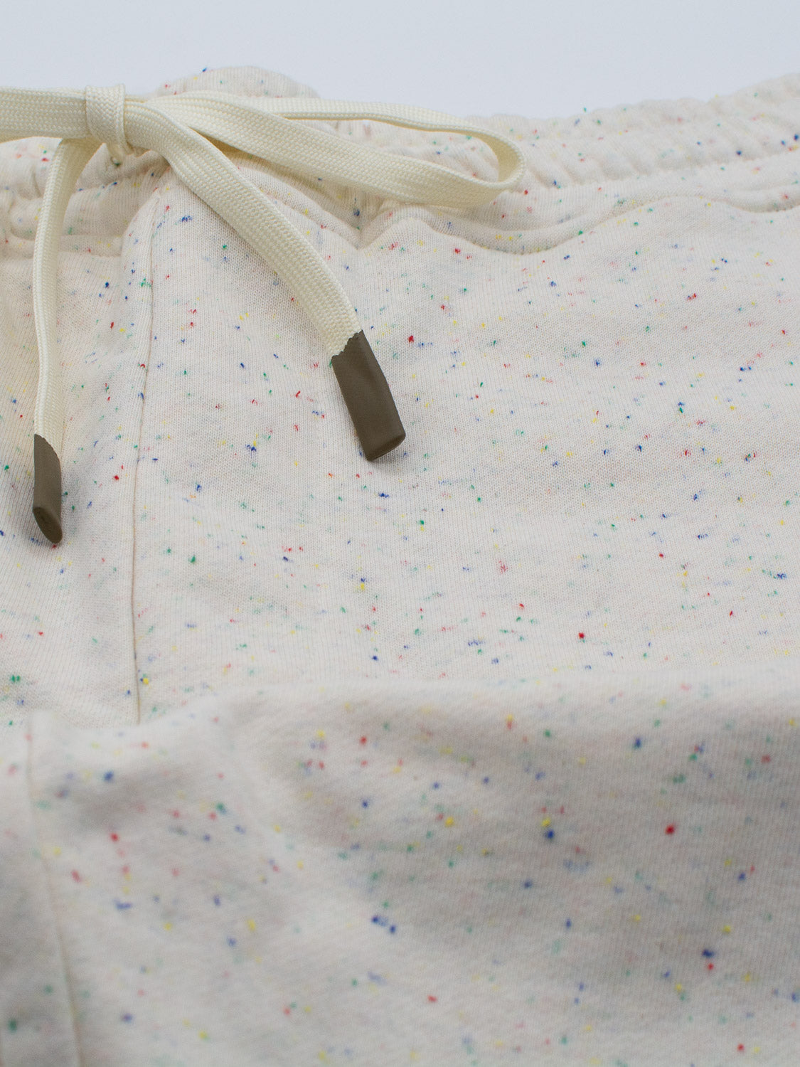 Close-up of ID Menswears Waikiki Speckled Cotton Shorts in off-white, crafted from speckled cotton yarn with a subtle multicolored pattern. The drawstring, featuring dark tips, is shown at the waistband, highlighting its casual and fashion-forward style.