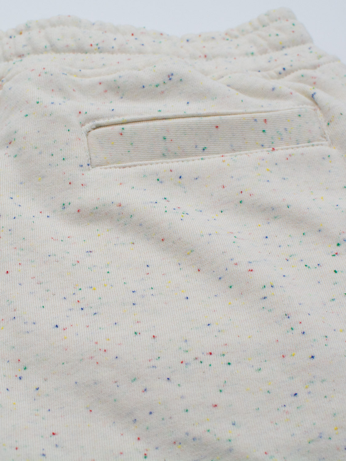 Close-up of Waikiki Speckled Cotton Shorts by ID Menswear in light beige with colorful red, blue, green, and yellow dots; highlights rear pocket detail and showcases the fabrics soft-textured, fashion-forward style.