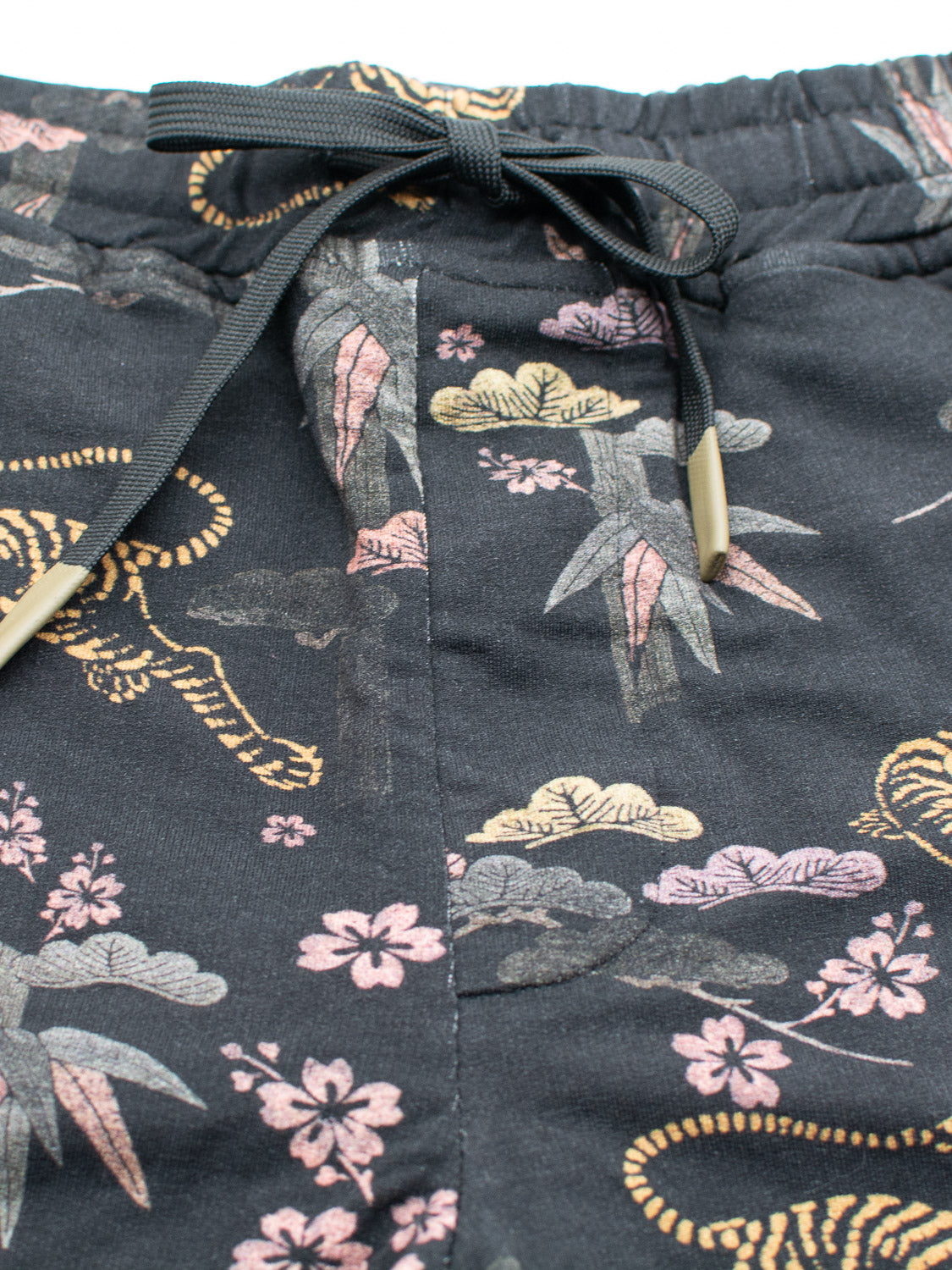 Close-up of black sweatpants featuring a bamboo and nature-inspired design in pink, yellow, and gray tones. The waistband includes a black drawstring with tan ends. Made from organic cotton, the fabric texture is beautifully visible. Product: Samui Vintage Japanese Print Short by ID Menswear.