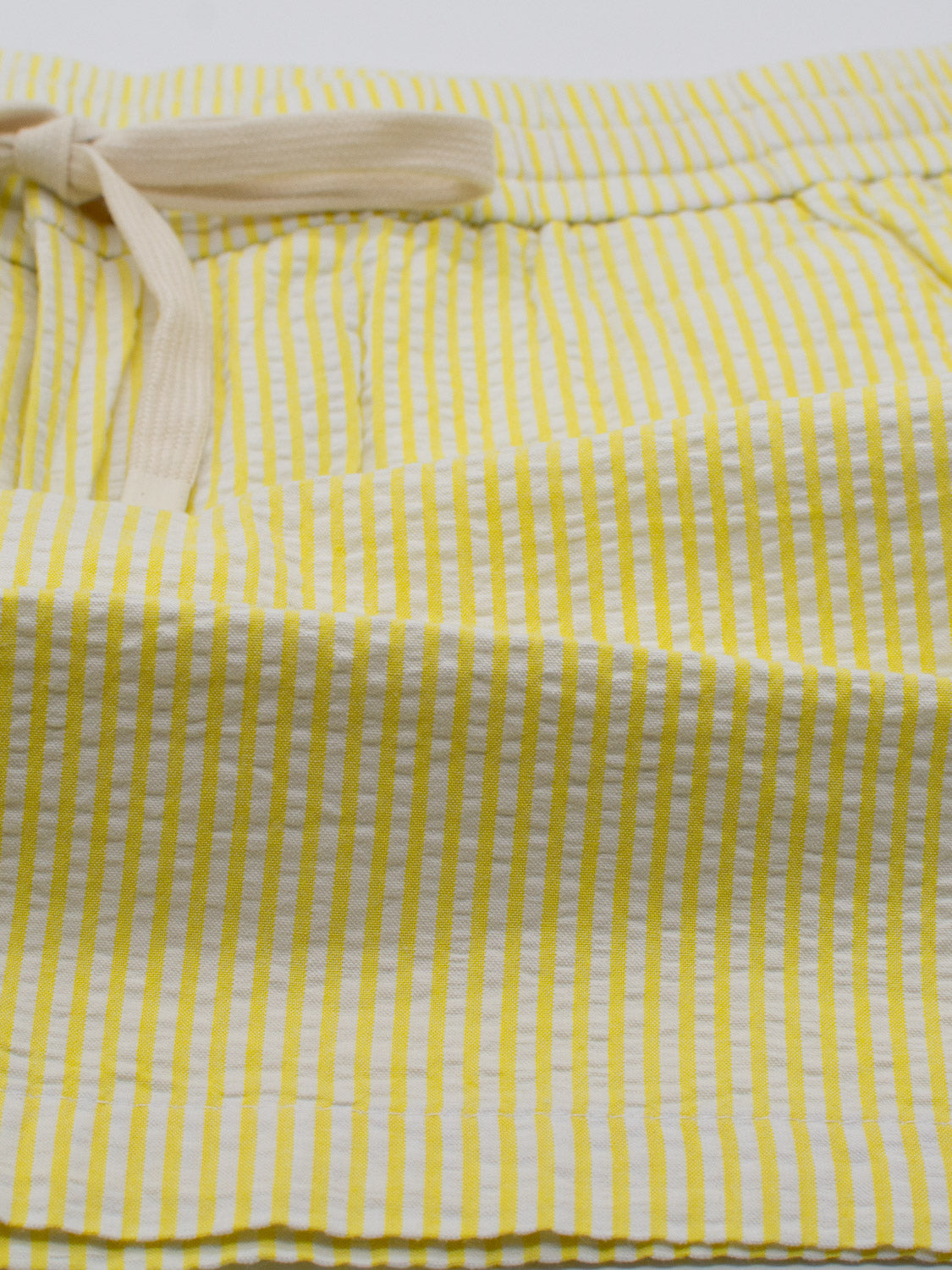 Close-up of ID Menswears Ibiza Seersucker Drawstring Short, showcasing yellow and white stripes. The lightweight, textured fabric makes it ideal for warm weather, perfect for both clothing and home textiles.