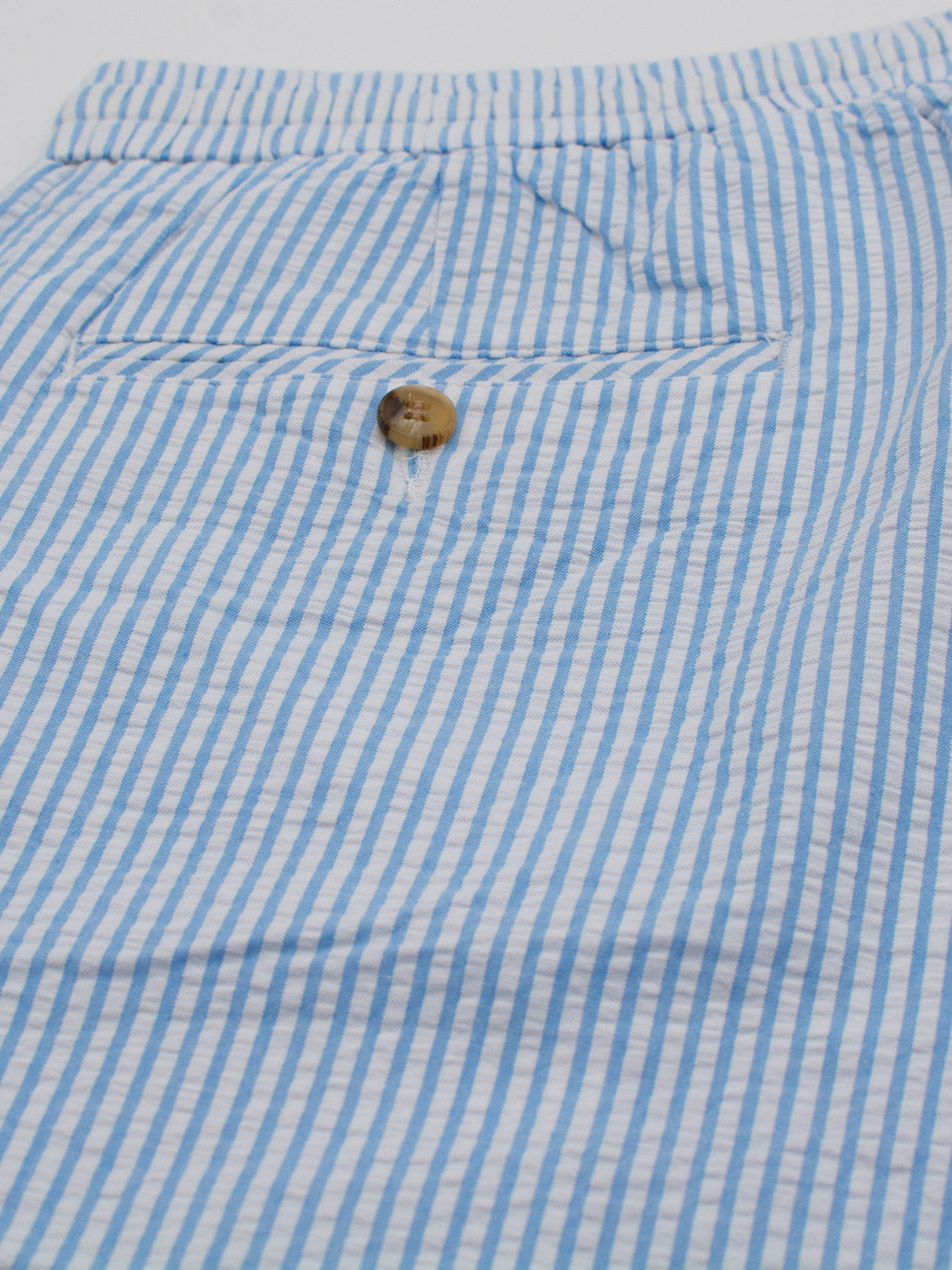 The Ibiza Seersucker Drawstring Short by ID Menswear showcases blue and white striped fabric with a single button above a slit pocket, adding a relaxed touch to your warm-weather wardrobe.