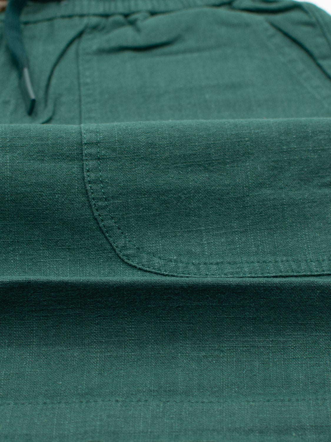Close-up of the Phi Phi Linen Blend Drawstring Short by ID Menswear, showcasing the green woven fabric with visible pocket detail and stitching. Features include a 6 inseam, elastic waistband, and partially visible drawstring at the top.