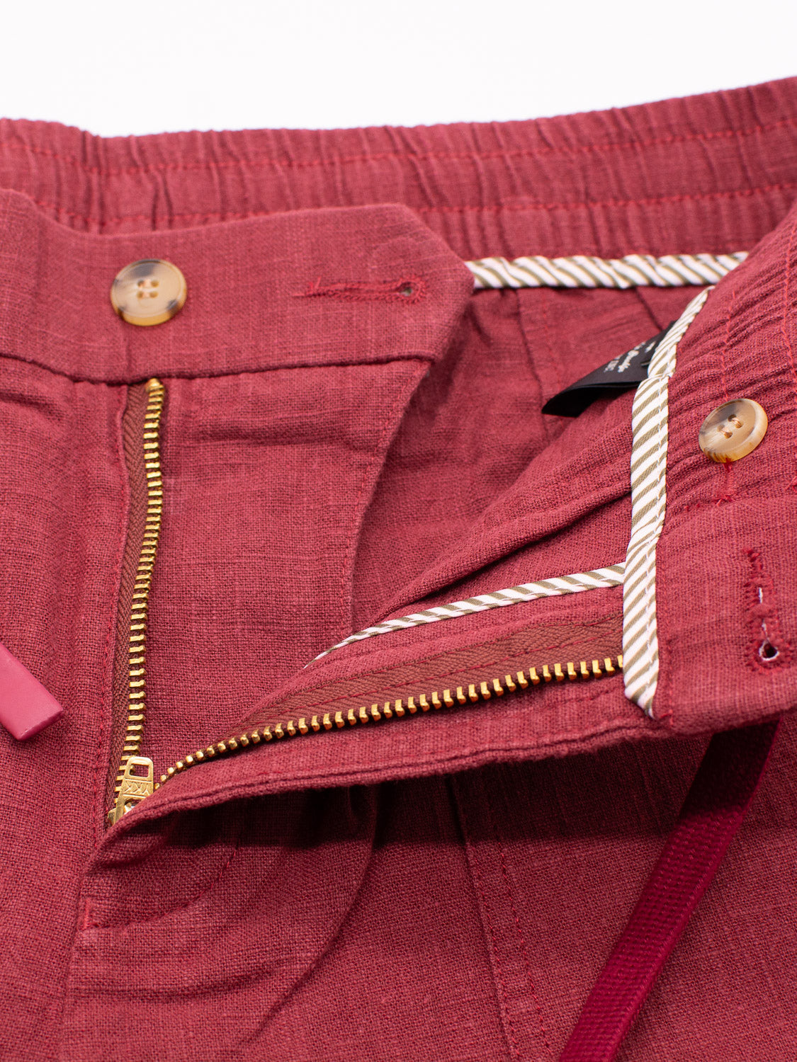 Close-up of ID Menswears red Phi Phi Linen Blend Drawstring Shorts features an open zipper fly, two brown buttons, a striped elastic waistband with a pink drawstring, and textured fabric with a stylish 6 inseam.