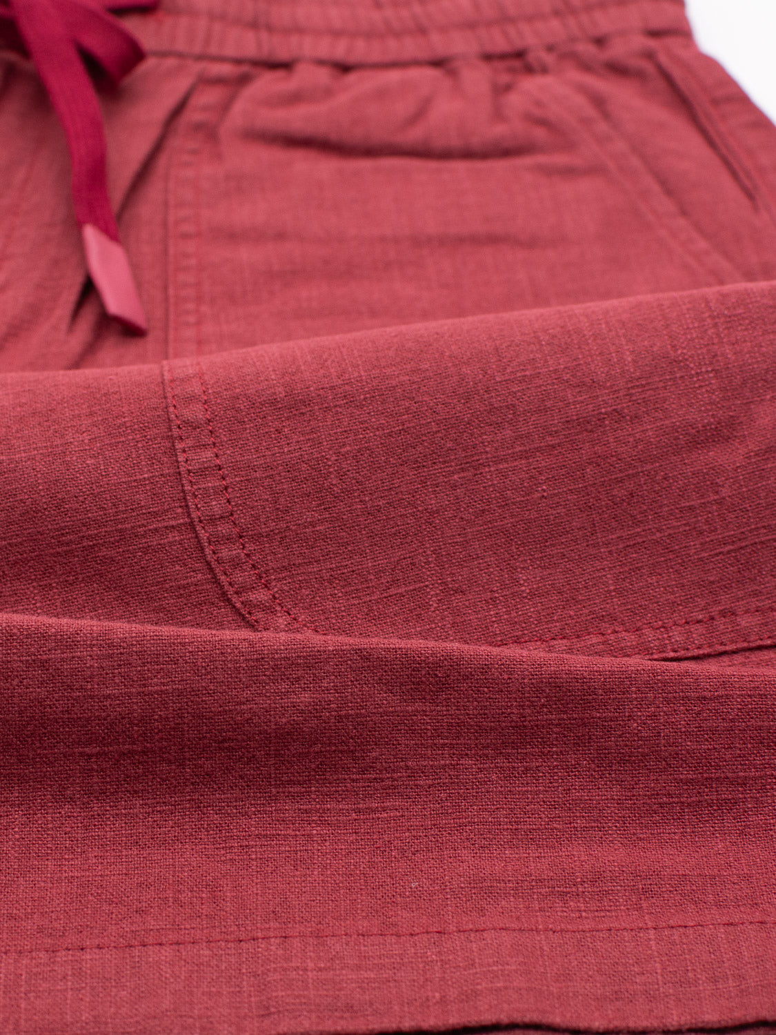 Close-up of the ID Menswear Phi Phi Linen Blend Drawstring Short, featuring a 6 inseam, elastic waistband, and drawstring. The fabric has visible stitching and a textured look in deep red with burgundy hints on the drawstring.