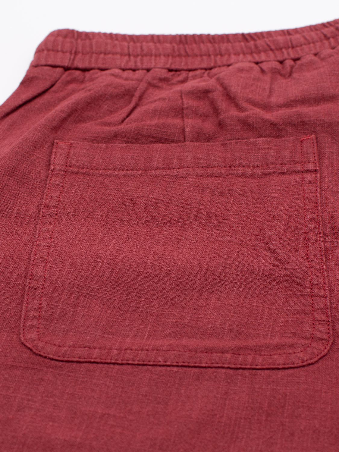 A close-up of the back pocket on ID Menswears red Phi Phi Linen Blend Drawstring Shorts reveals textured, lightweight linen with an elastic waistband and neatly stitched pocket matching the fabrics color.