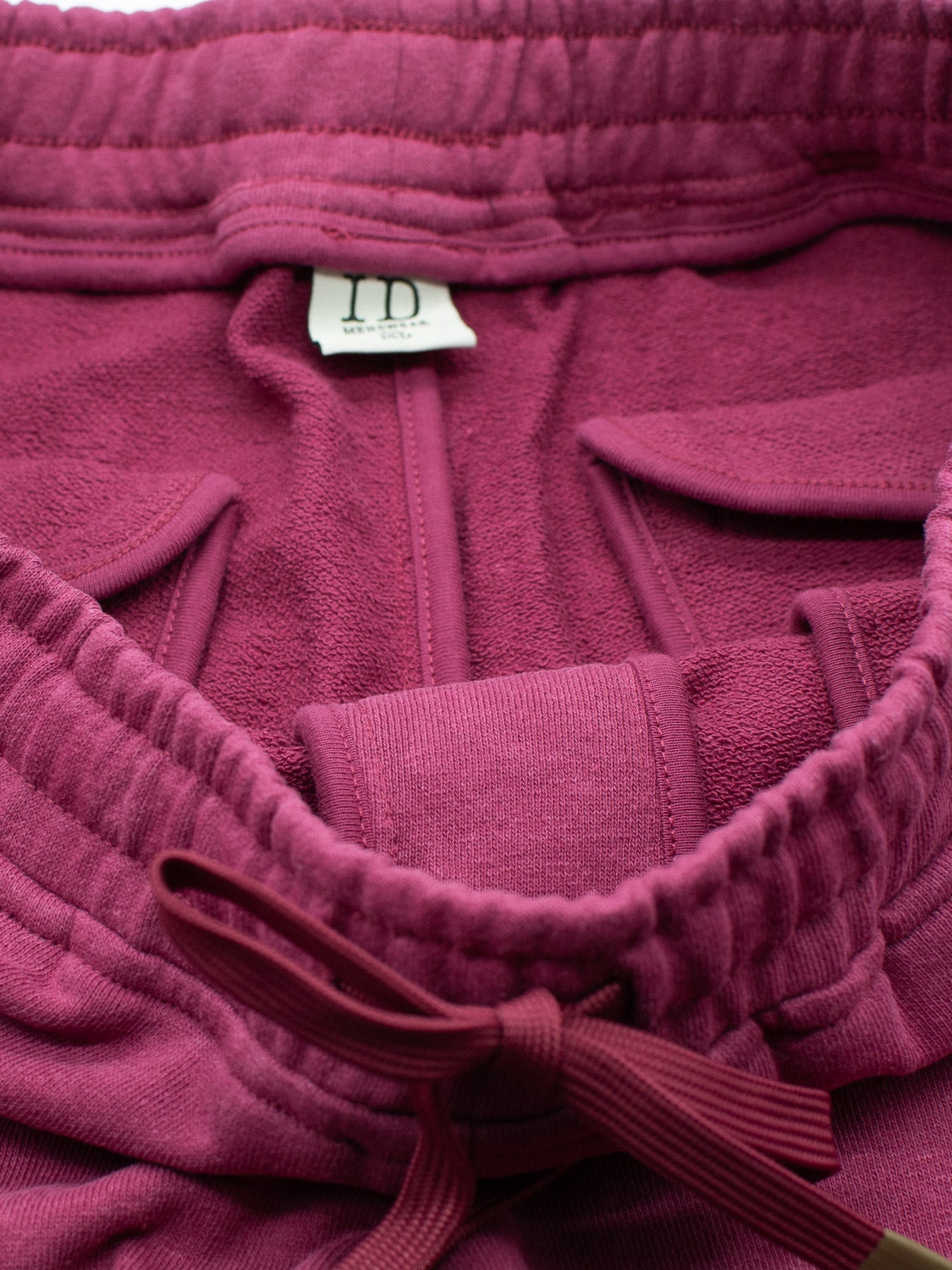 Close-up of the Walker Hemp Cotton Terry Short by ID Menswear, featuring an elastic waistband with a drawstring. A small white label with washing instructions contrasts against the maroon terry cloth fabric.