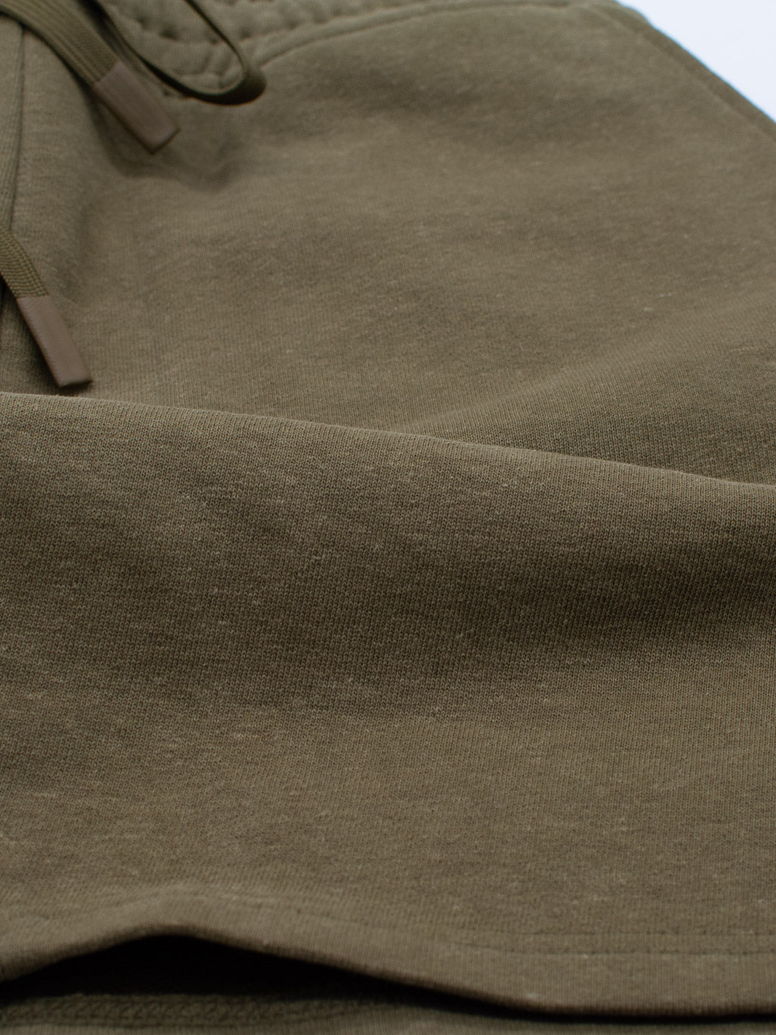 Close-up of a textured olive green fabric with a drawstring, suggesting its part of the Walker Hemp Cotton Terry Short by ID Menswear. The material looks soft and slightly wrinkled.