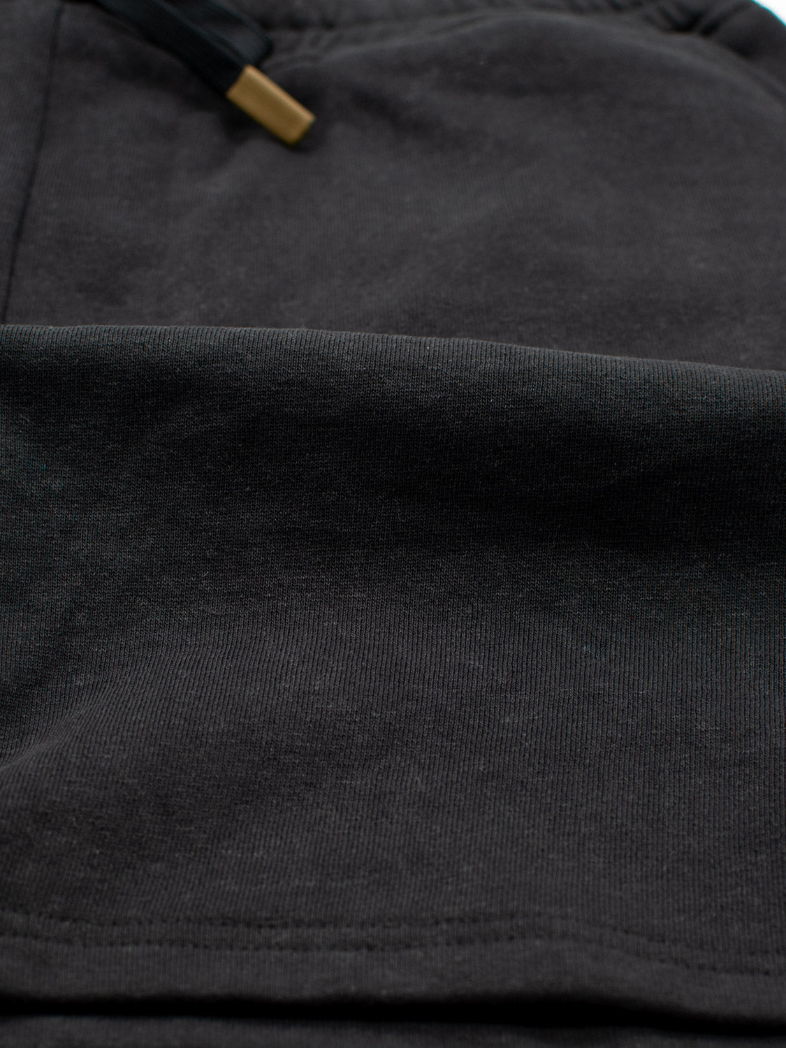 Close-up of black Walker Hemp Cotton Terry Short by ID Menswear, highlighting textured fabric and a black drawstring with a gold tip. The smooth, slightly folded material embodies comfort and style, akin to the luxury found in organic cotton shorts.