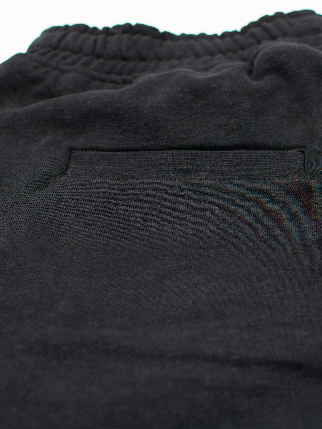 Close-up of Walker Hemp Cotton Terry Short by ID Menswear, showcasing dark-colored pants with an elastic waistband above a single back pocket. The soft, slightly textured fabric is crafted from organic cotton.