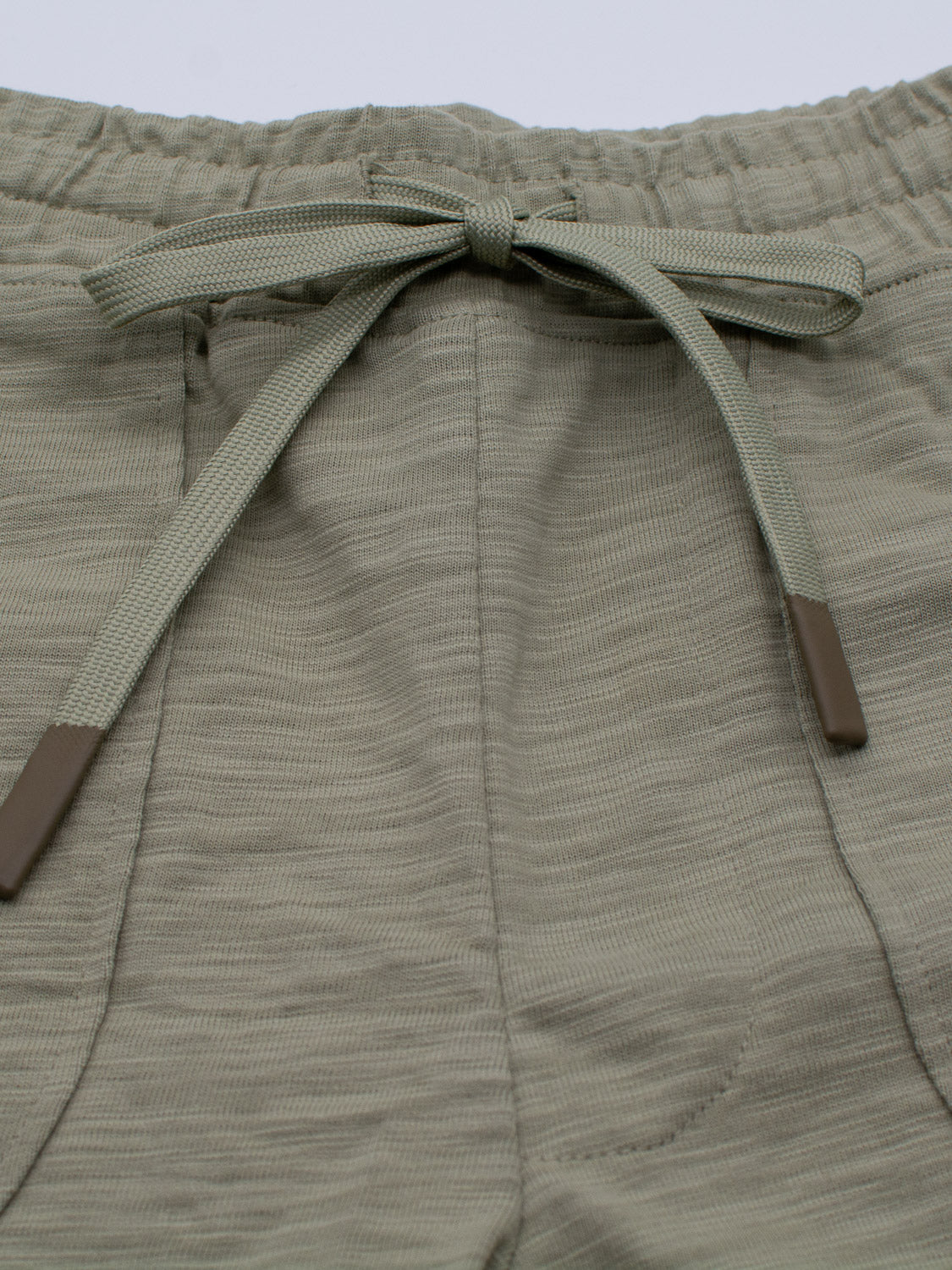 Close-up of the Kahala Slub Cotton Drawstring Short by ID Menswear in olive green, showcasing a relaxed fit and an elastic waistband with tied drawstring. The textured, crinkled slub cotton fabric and brown plastic tips on the drawstring complete the look.
