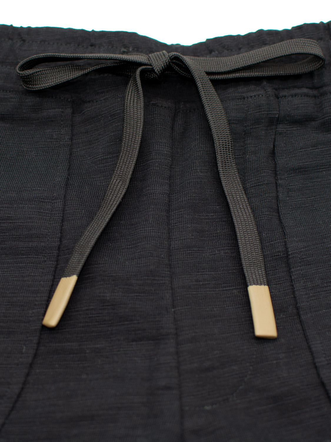 A close-up of the Kahala Slub Cotton Drawstring Short by ID Menswear shows black fabric pants with a relaxed fit and subtle textured pattern, featuring an adjustable drawstring waist with beige tips.