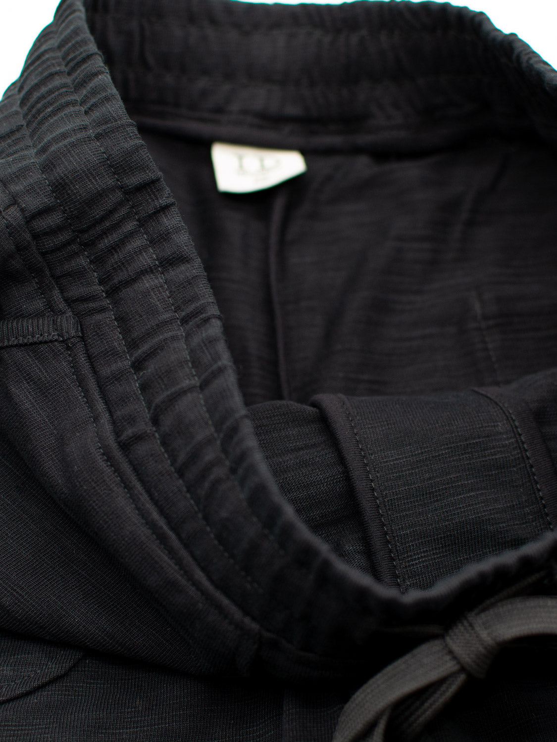 A close-up of the Kahala Slub Cotton Drawstring Short by ID Menswear in black, made from sturdy slub cotton fabric. The relaxed fit is designed for comfort during training and features a label inside.