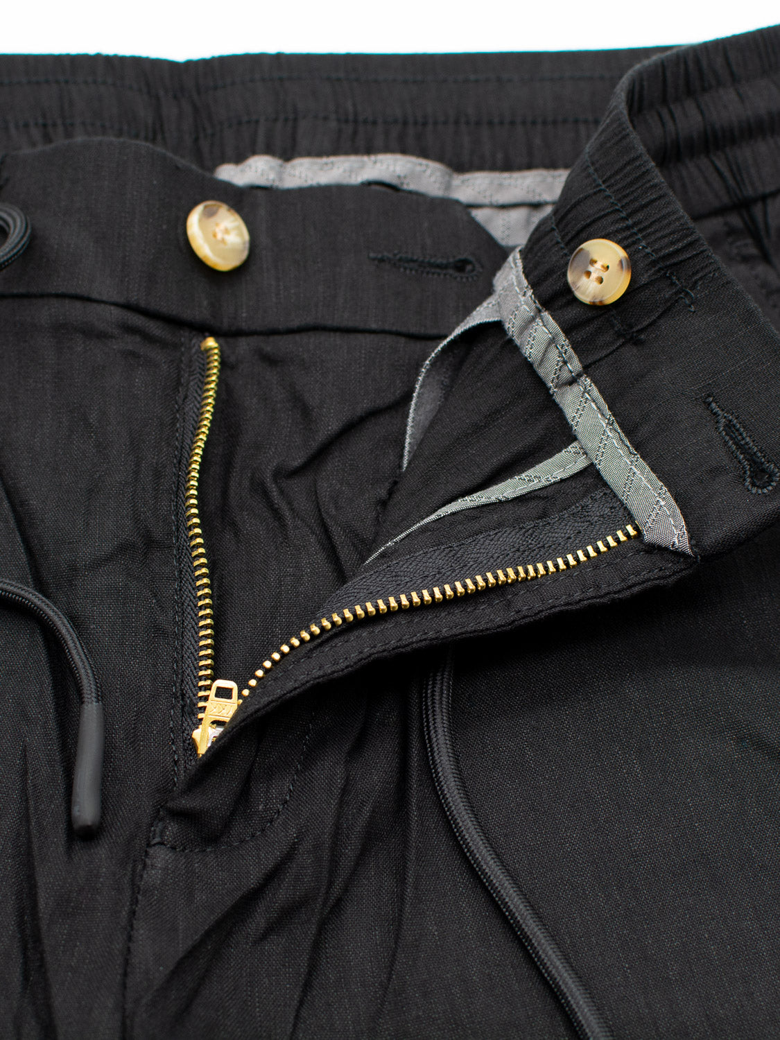 Close-up of Driggs Linen Blend Short by ID Menswear, featuring a black exterior with a partially open zipper and buttoned waistband. The contrasting gray lining, detailed stitching, and string drawcords ensure comfort in warm weather.