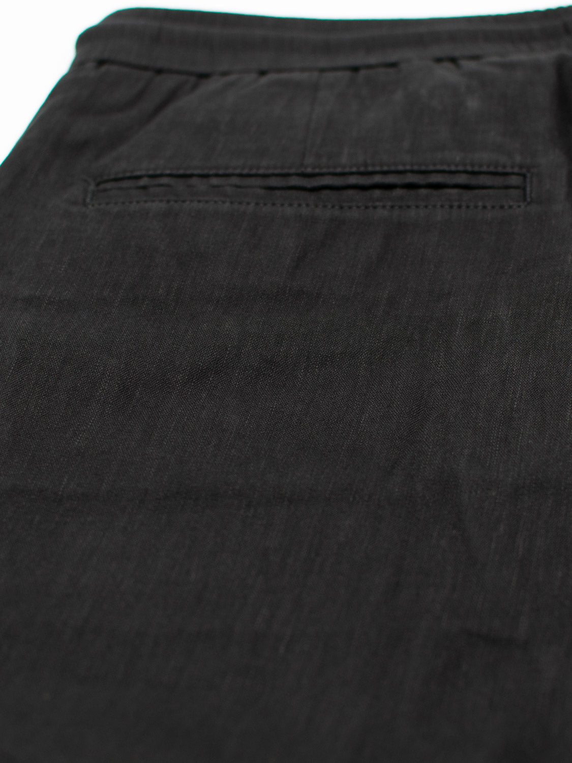 A close-up of the Driggs Linen Blend Short by ID Menswear reveals a textured fabric and horizontal slit back pocket with no visible buttons. Soft lighting showcases its details, making these black shorts ideal for warm weather while ensuring a comfortable fit.