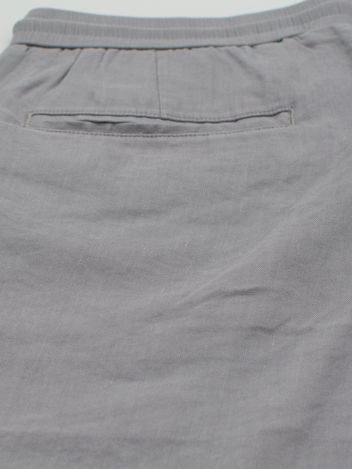 A close-up of Driggs Linen Blend Shorts by ID Menswear highlights a rear pocket with a horizontal opening. The gray, soft, slightly wrinkled linen-blend fabric offers a casual design ideal for warm weather comfort.