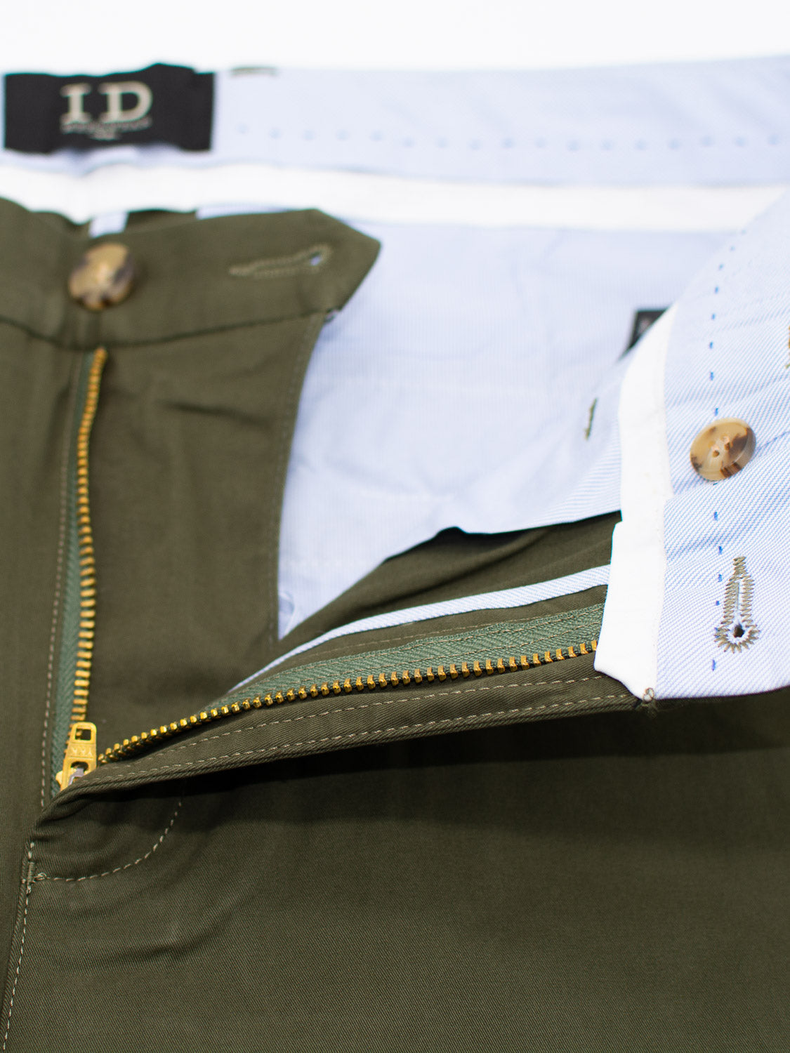 Close-up of At Ease Relaxed Chino Short in green with the zipper partly undone, showing a light blue waistband. The chinos feature brown buttons, and the ID Menswear label is visible at the top.