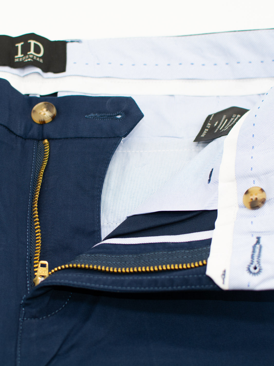 The At Ease Relaxed Chino Short by ID Menswear showcases a navy blue interior with gold zipper, visible label, white lining, and branded button closures. The waistbands striped pattern and contrast stitching add both style and comfort.