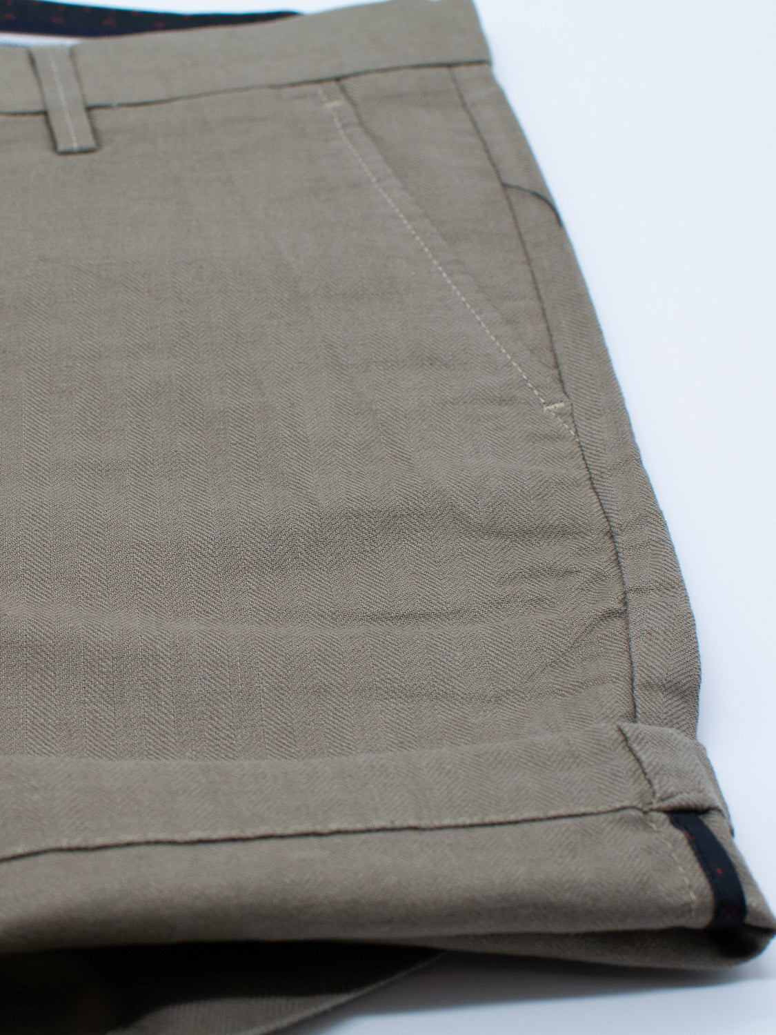A close-up of the Kerala Linen Blend Chino Short from ID Menswear reveals their relaxed fit with folded hem and visible stitching. The linen-cotton blend fabric features a subtle textured pattern, belt loops add a finishing touch, and they exude casual sophistication on a white background.