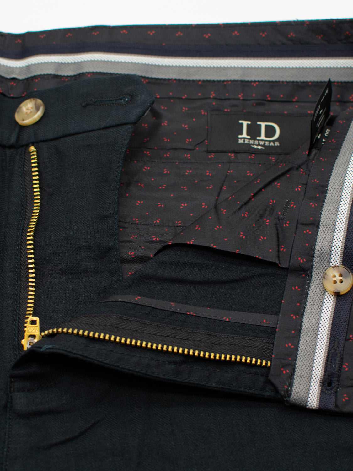 Close-up of a pair of mens Kerala Linen Blend Chino Shorts by ID Menswear, featuring a visible zipper and button closure. The inner waistband displays dotted patterned fabric and tag. These dark-colored shorts are made from a linen-cotton blend for relaxed fit suitable for any occasion.