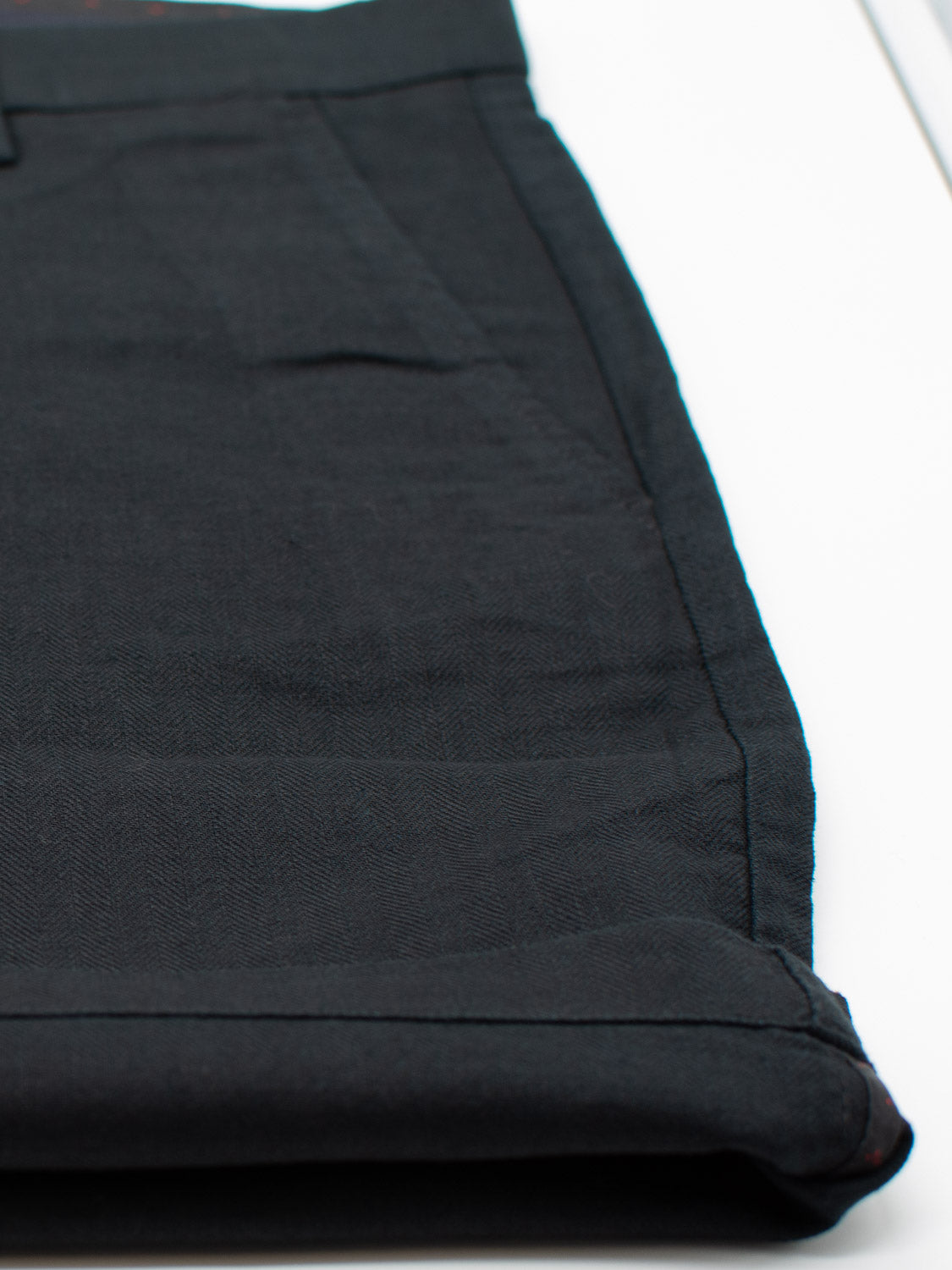 A close-up of neatly folded Kerala Linen Blend Chino Shorts by ID Menswear on a white surface highlights the fabric texture and stitching, with one pocket slightly open.