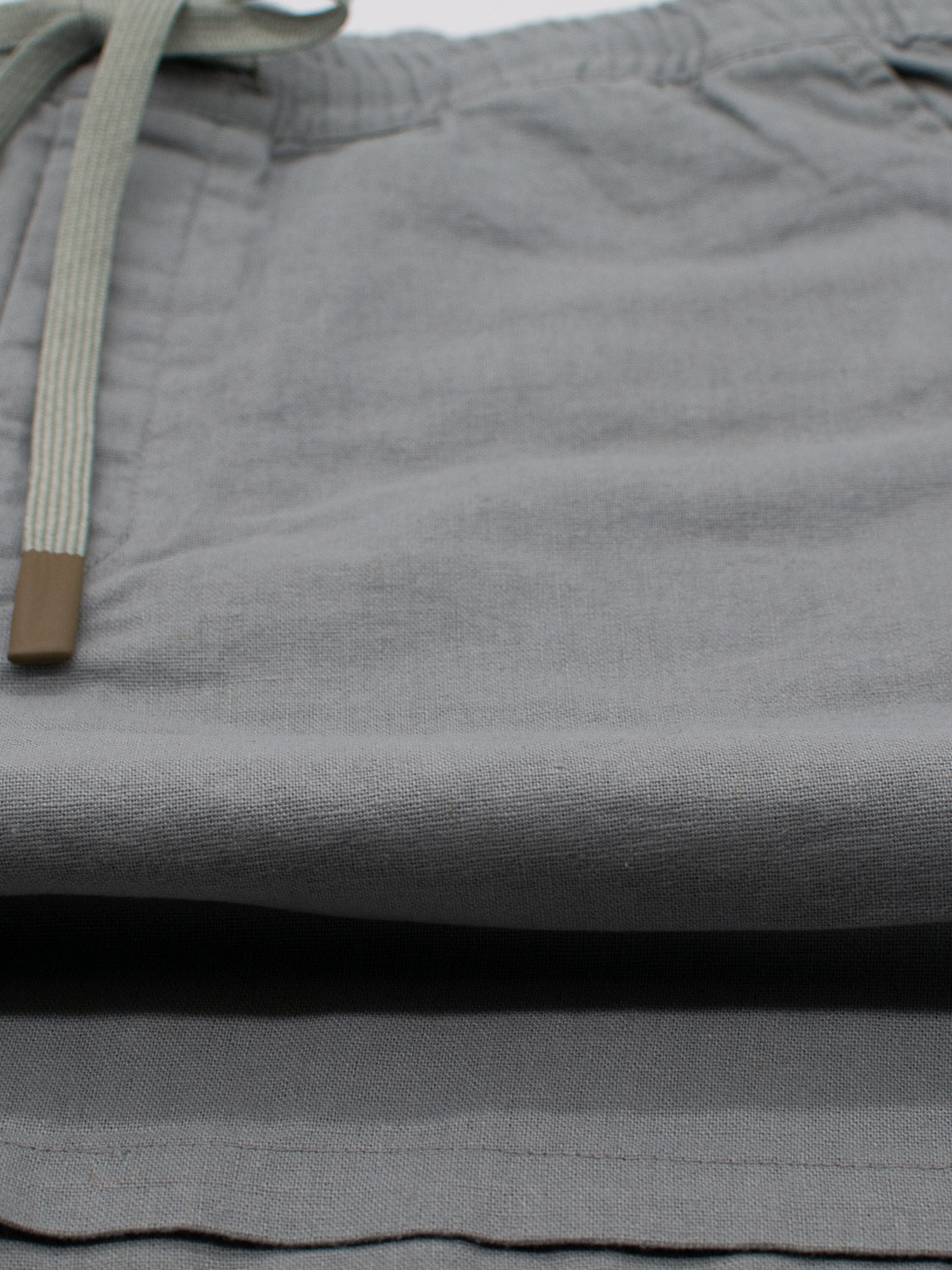Close-up of Kotao Linen Blend Drawstring Short by ID Menswear in light gray. Features elastic waistband with light green drawstring. Soft, lightweight fabric perfect for warm weather comfort.