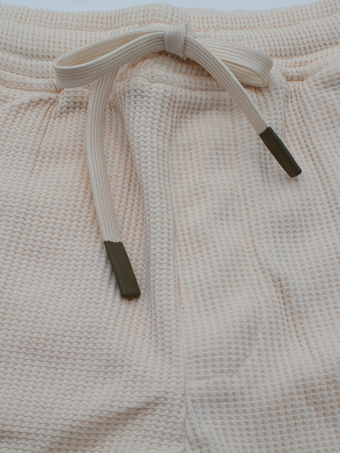 Close-up of the Walker Waffle Knit Shorts by ID Menswear, featuring a beige waffle texture. These organic cotton shorts have a white drawstring with dark tips knotted at the center, offering a casual and comfortable look.