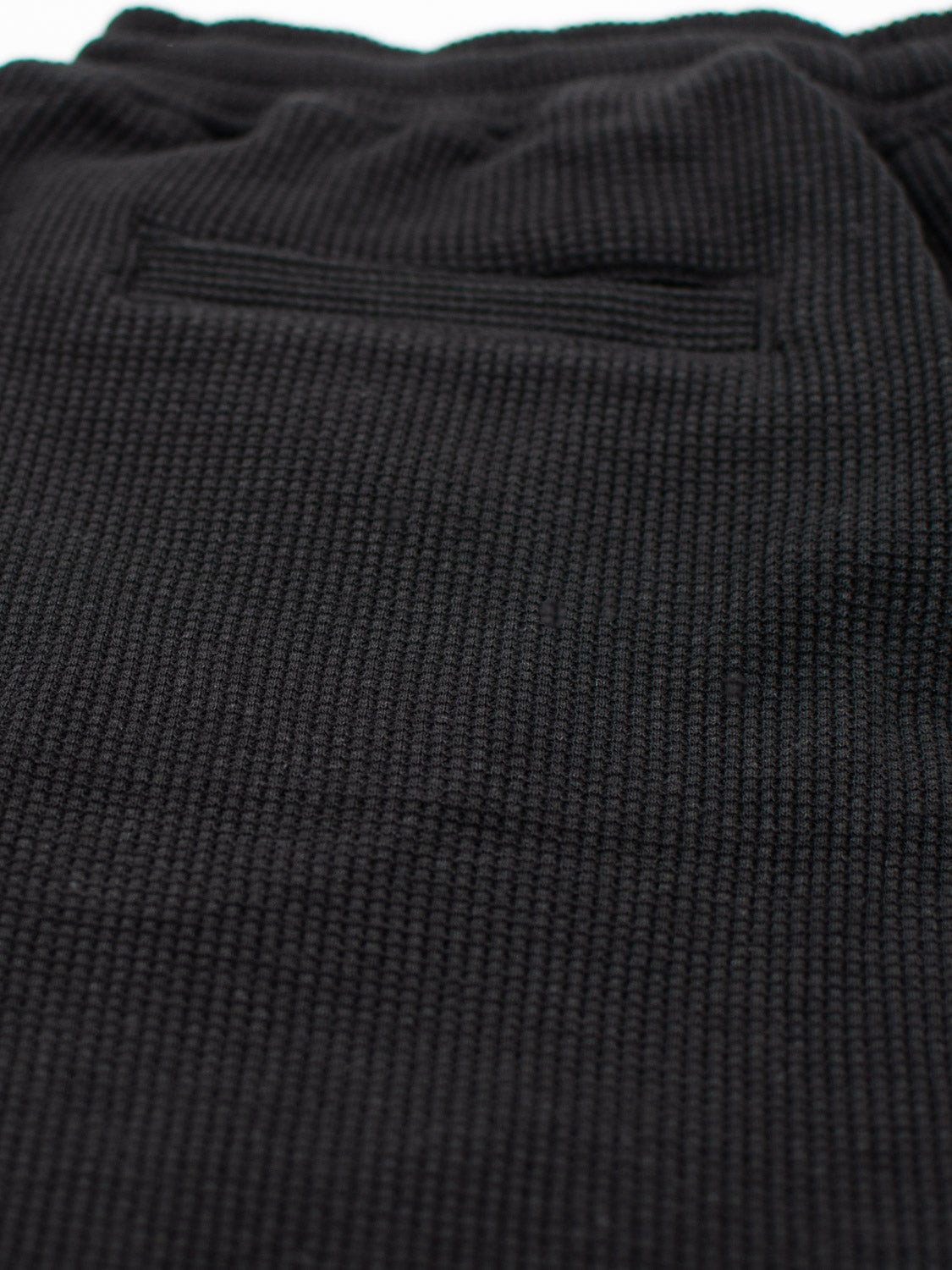 Close-up of the Walker Waffle Knit Short from ID Menswear in black, featuring a textured fabric and a small rectangular pocket near the top. The woven pattern adds both stylish depth and functional dimension to its appearance.