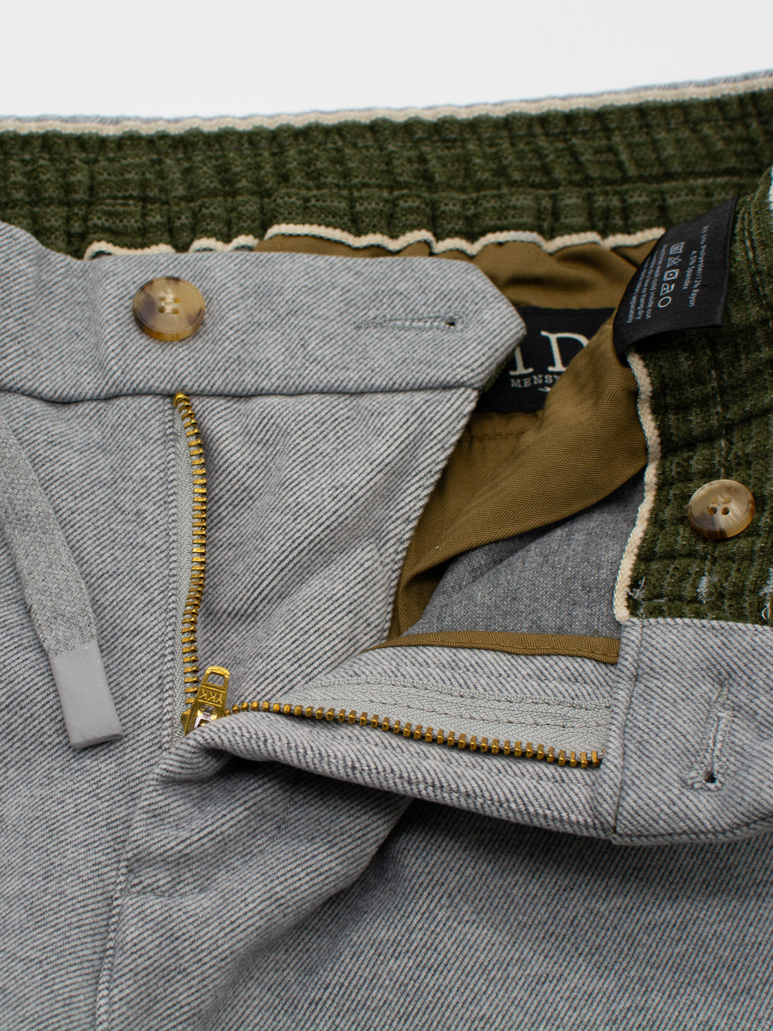 A close-up of the Brighton Brushed Polyester Rayon Pant by ID Menswear reveals gray drawstring pants with an open zipper, button fly, and two brown buttons. The green elastic waistband has a convenient drawstring and features a visible brand label inside.
