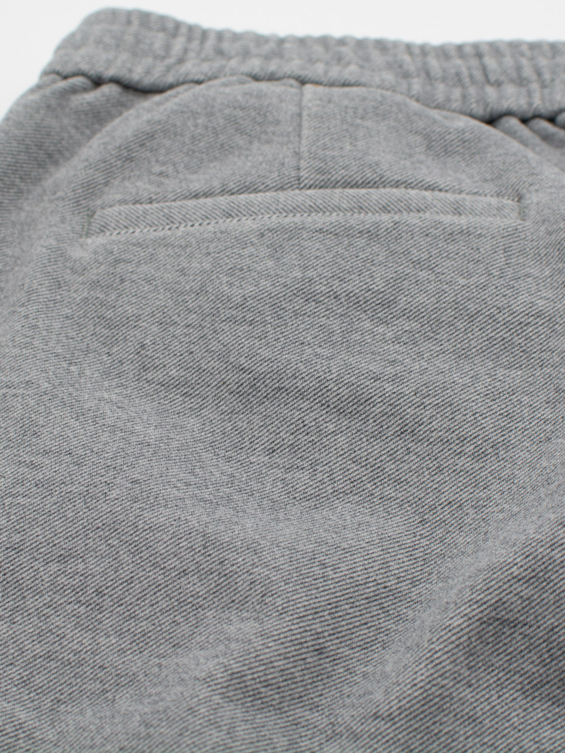 Close-up of the Brighton Brushed Polyester Rayon Pant by ID Menswear, showcasing a gray fabric with a pocket and subtle seam. The texture appears soft, ideal for casual wear like sweatpants or drawstring pants.