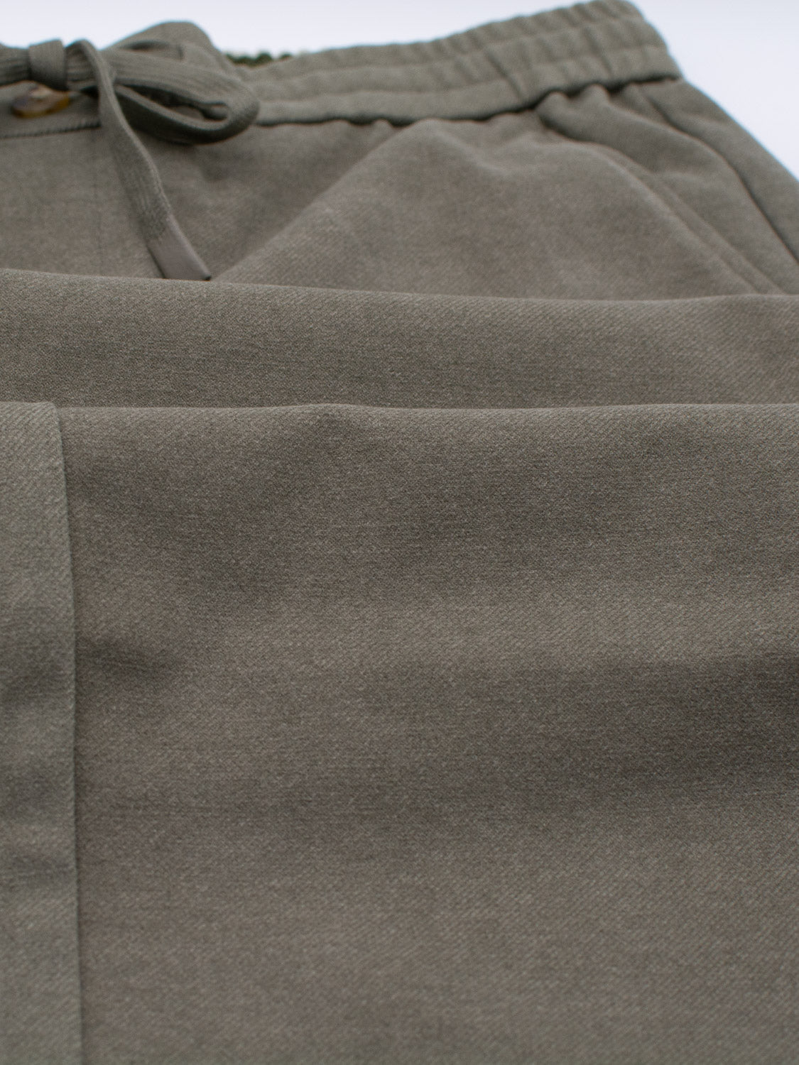 Close-up of ID Menswears Brighton Brushed Polyester Rayon Pant in olive green, highlighting an elastic waistband and drawstring. The fabric looks soft and comfortable, showcasing detailed visible seams and stitching.