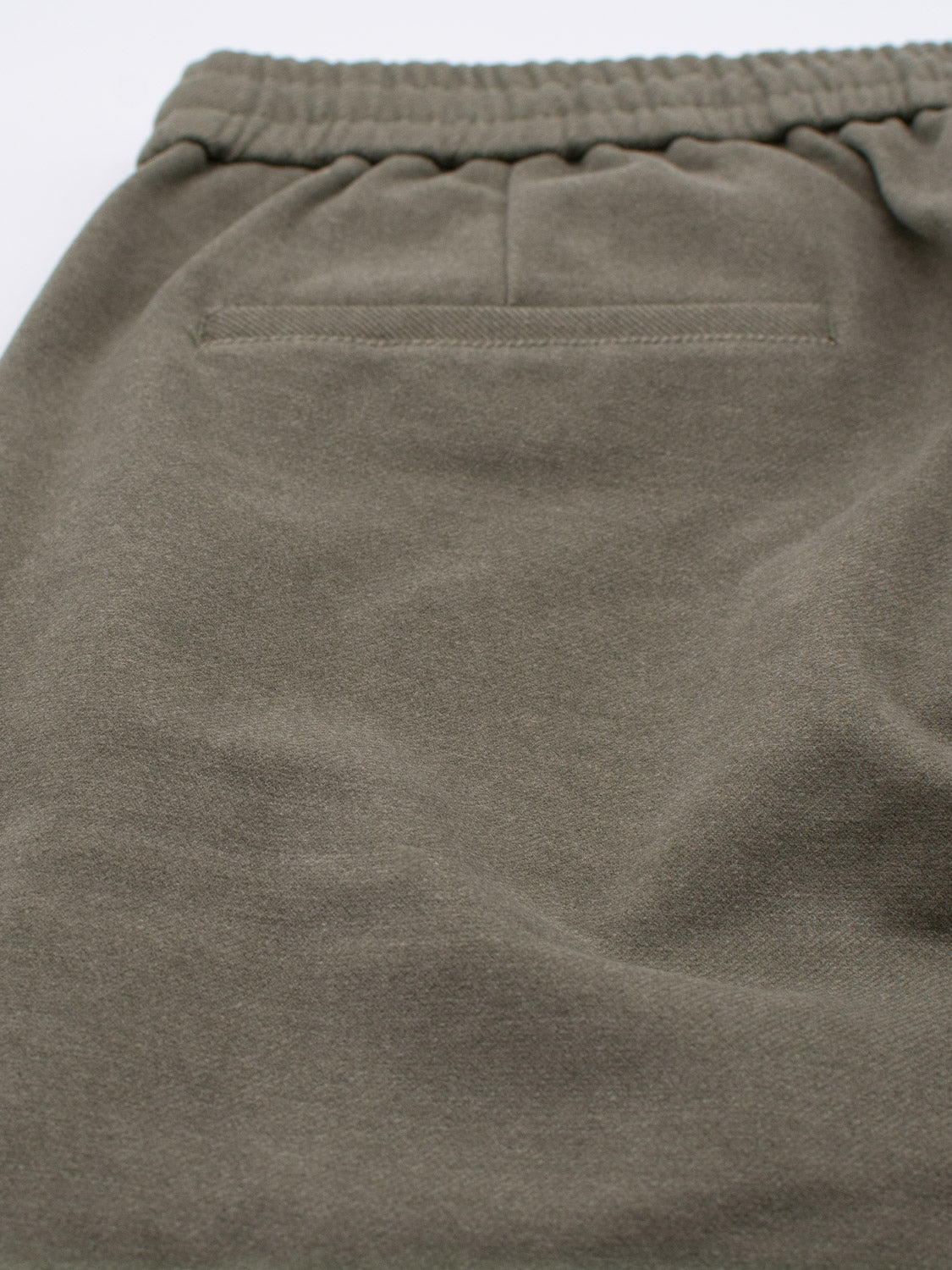 Close-up of an olive green fabric with subtle texture, spotlighting the elastic waistband and small welt-style pocket of the Brighton Brushed Polyester Rayon Pant by ID Menswear, combining style and comfort.