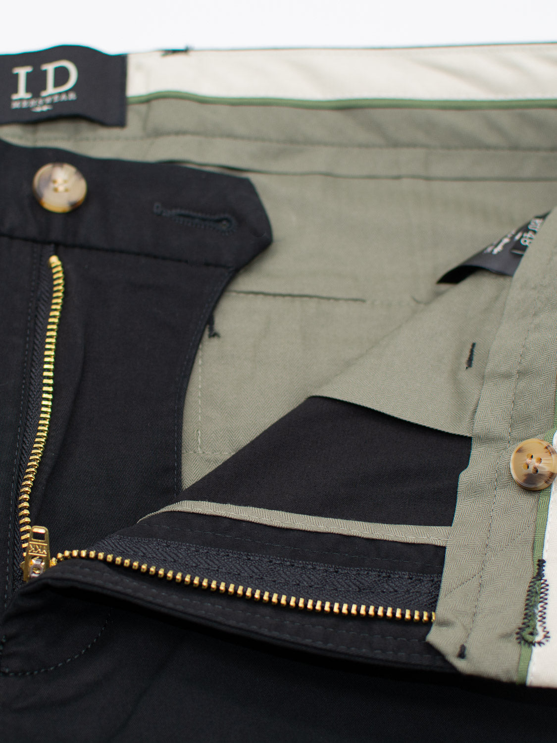 Close-up of ID Menswears Bigboy Relaxed Flooded Chino showcasing intricate inside details. The partially open zipper is beneath a button closure, featuring a relaxed, baggy fit with contrasting olive green and black interior fabric, complete with a visible waistband label for added style.