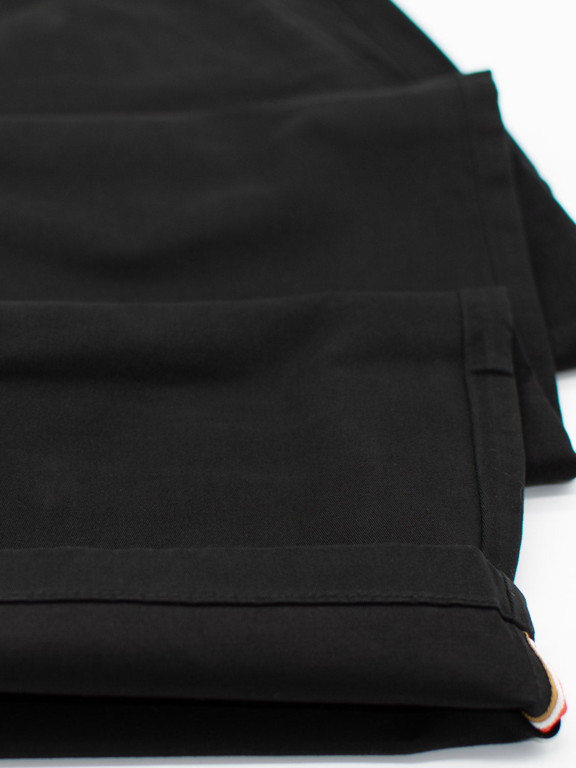 Close-up of the cuffed hem of black trousers on a white background, featuring sturdy fabric and a neat fold. This showcases the clean, polished finish typical of the Bigboy Relaxed Flooded Chino by ID Menswear, known for its relaxed, baggy fit.