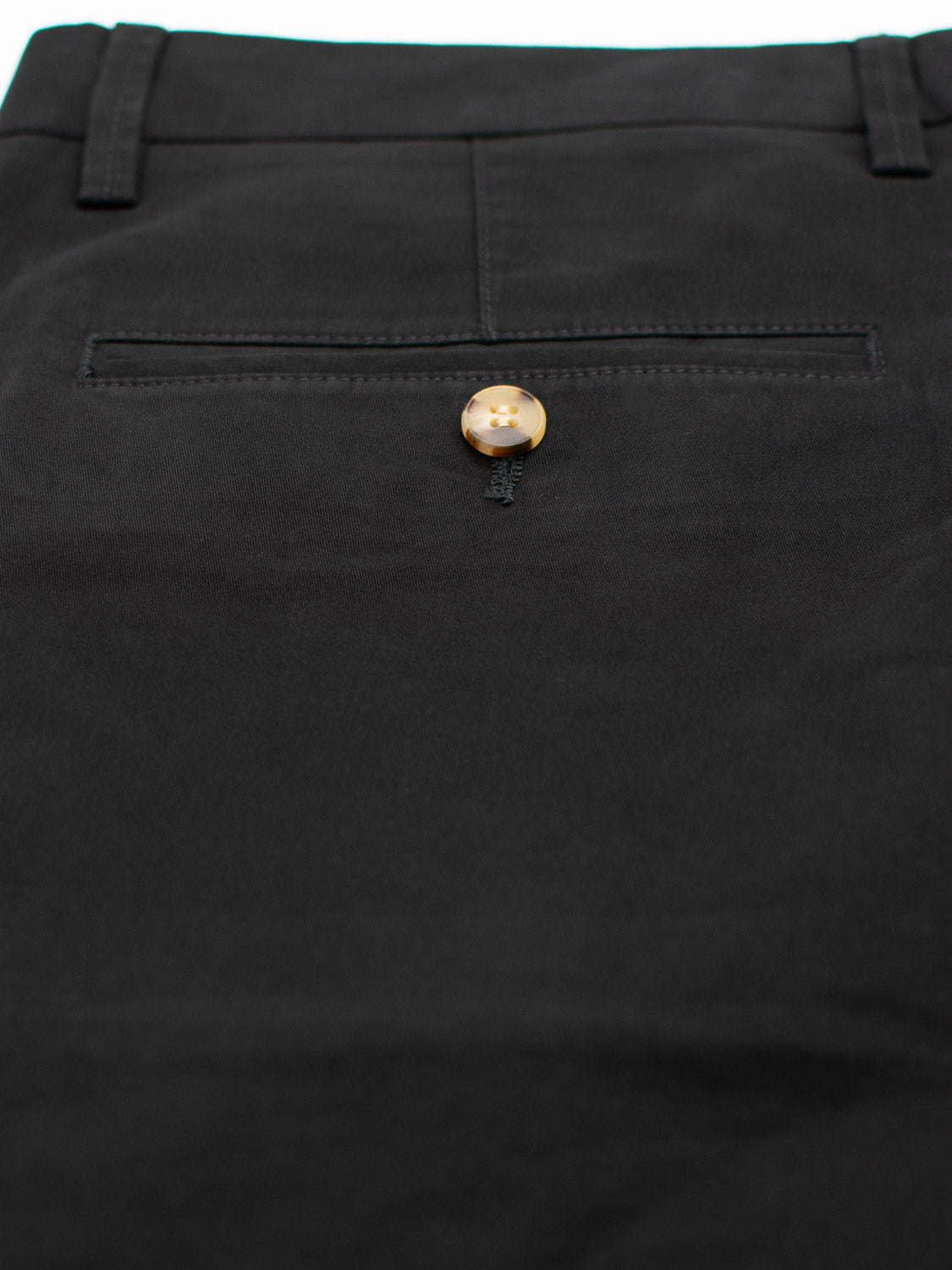 Close-up of black Bigboy Relaxed Flooded Chino by ID Menswear, featuring a back pocket with a brown button. The fabric is lightweight and flexible, offering a smooth and well-tailored look for a neat and polished design.