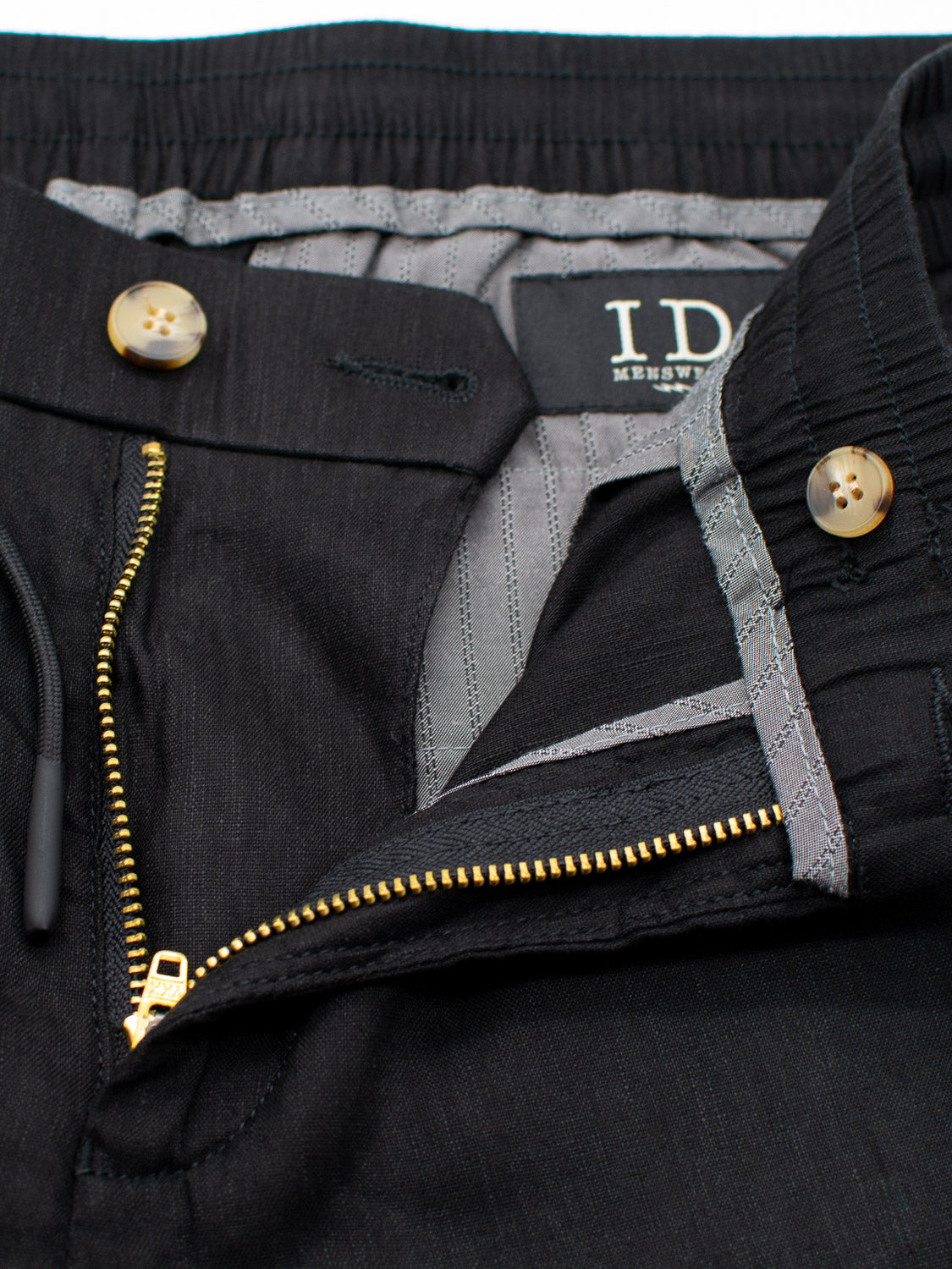Close-up of the ID Menswear Bedford23 Linen Blend Drawstring Pant featuring a visible gold zipper and buttons, with a slightly open elastic waistband revealing a gray striped inner lining.
