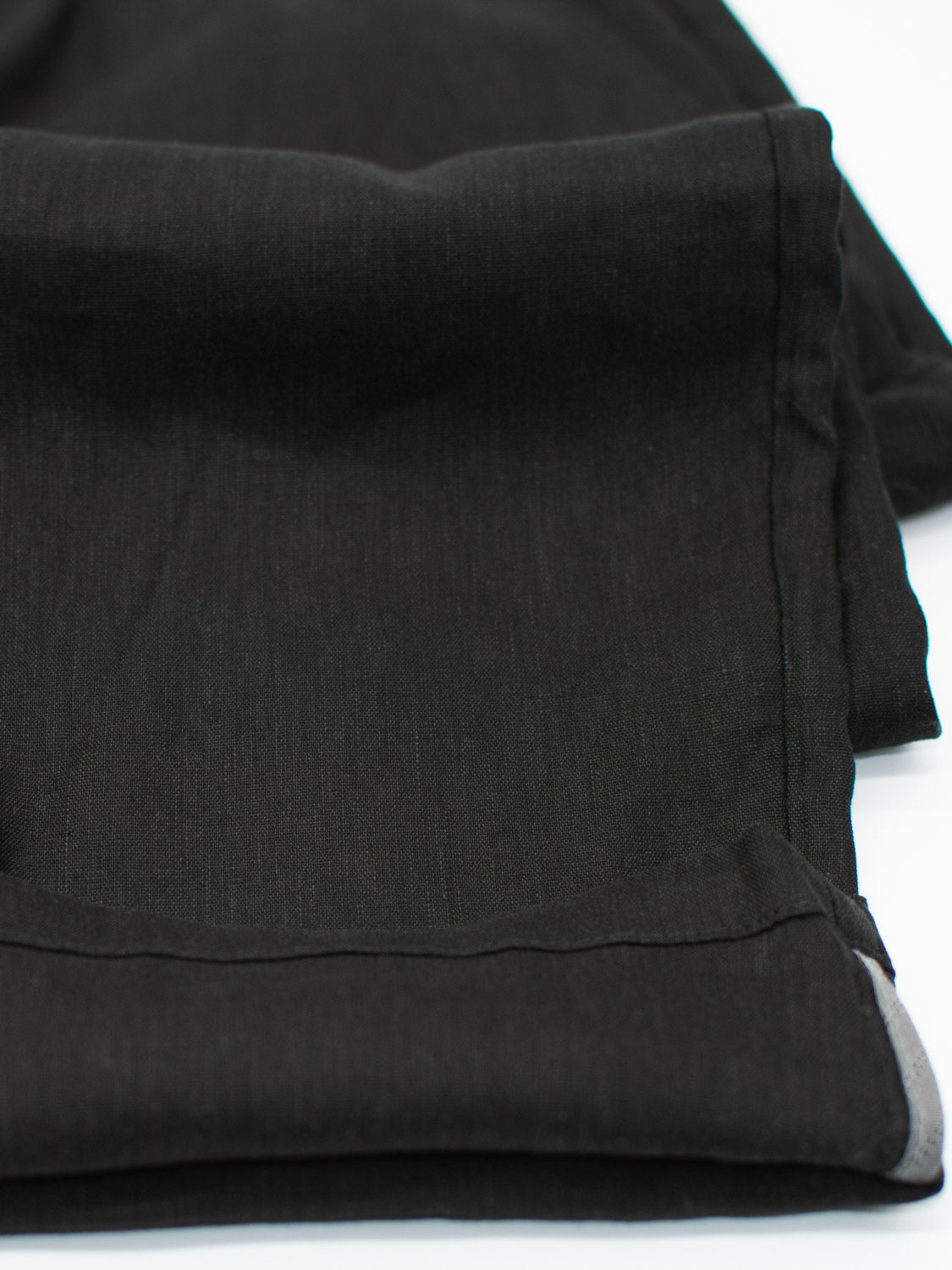 Close-up of folded black fabric highlighting its texture and weave, akin to the thick, smooth Bedford23 Linen Blend Drawstring Pant by ID Menswear, featuring neatly hemmed edges.