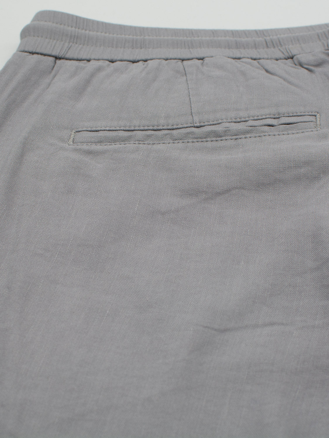 Close-up of the back of light gray ID Menswears Bedford23 Linen Blend Drawstring Pant, showcasing an elastic drawstring waistband and a single horizontal pocket. The lightweight, slightly wrinkled fabric appears soft, ensuring comfort for everyday wear.