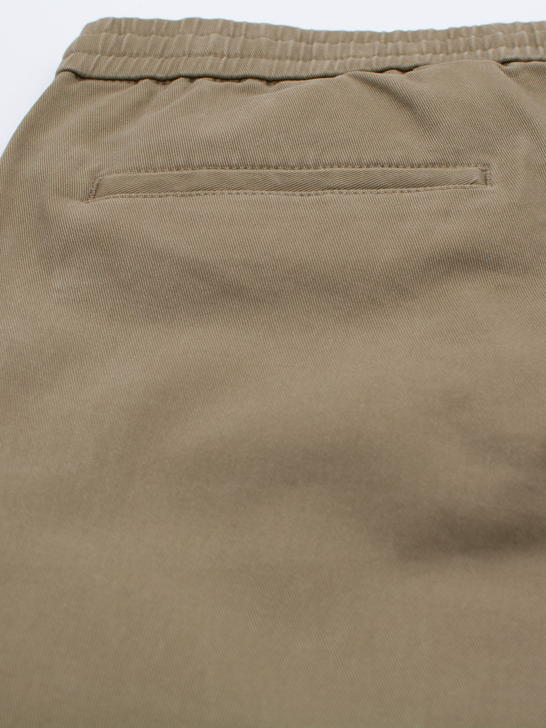 Close-up of the Dyker Cotton Twill Drawstring Jogger by ID Menswear, featuring beige fabric with a single back pocket. The material is slightly textured, and the pocket has a horizontal opening typical of elastic-waist joggers.