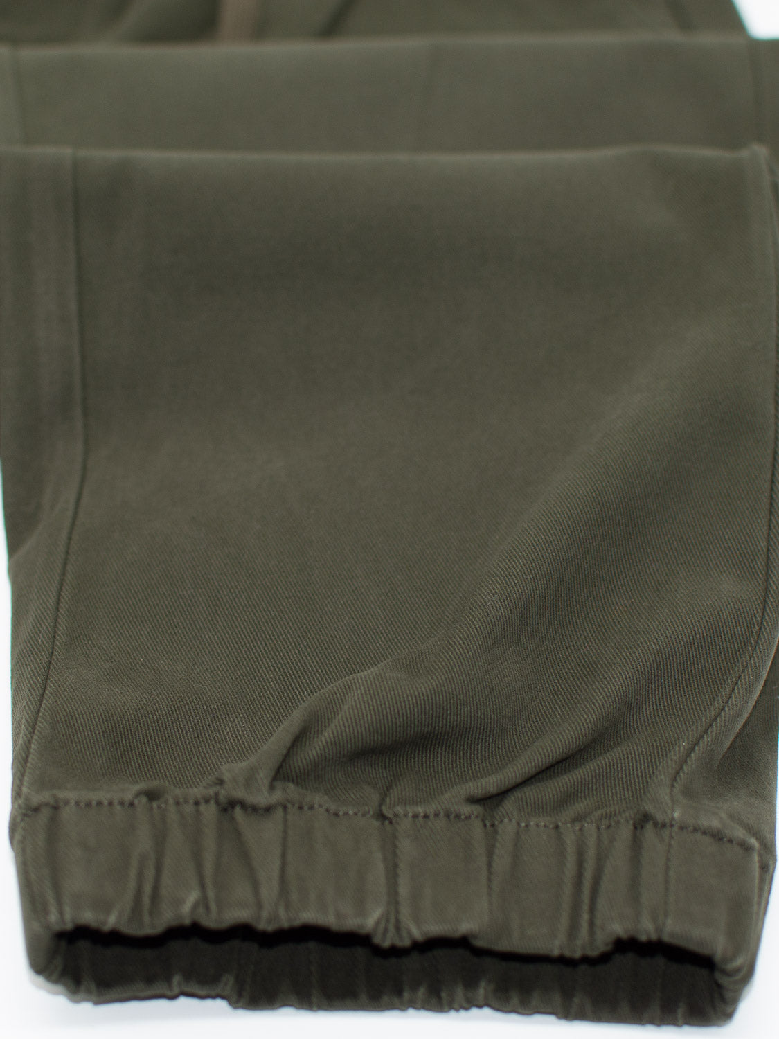 A detailed close-up of the Dyker Cotton Twill Drawstring Jogger from ID Menswear illustrates its olive green texture and elastic hem.