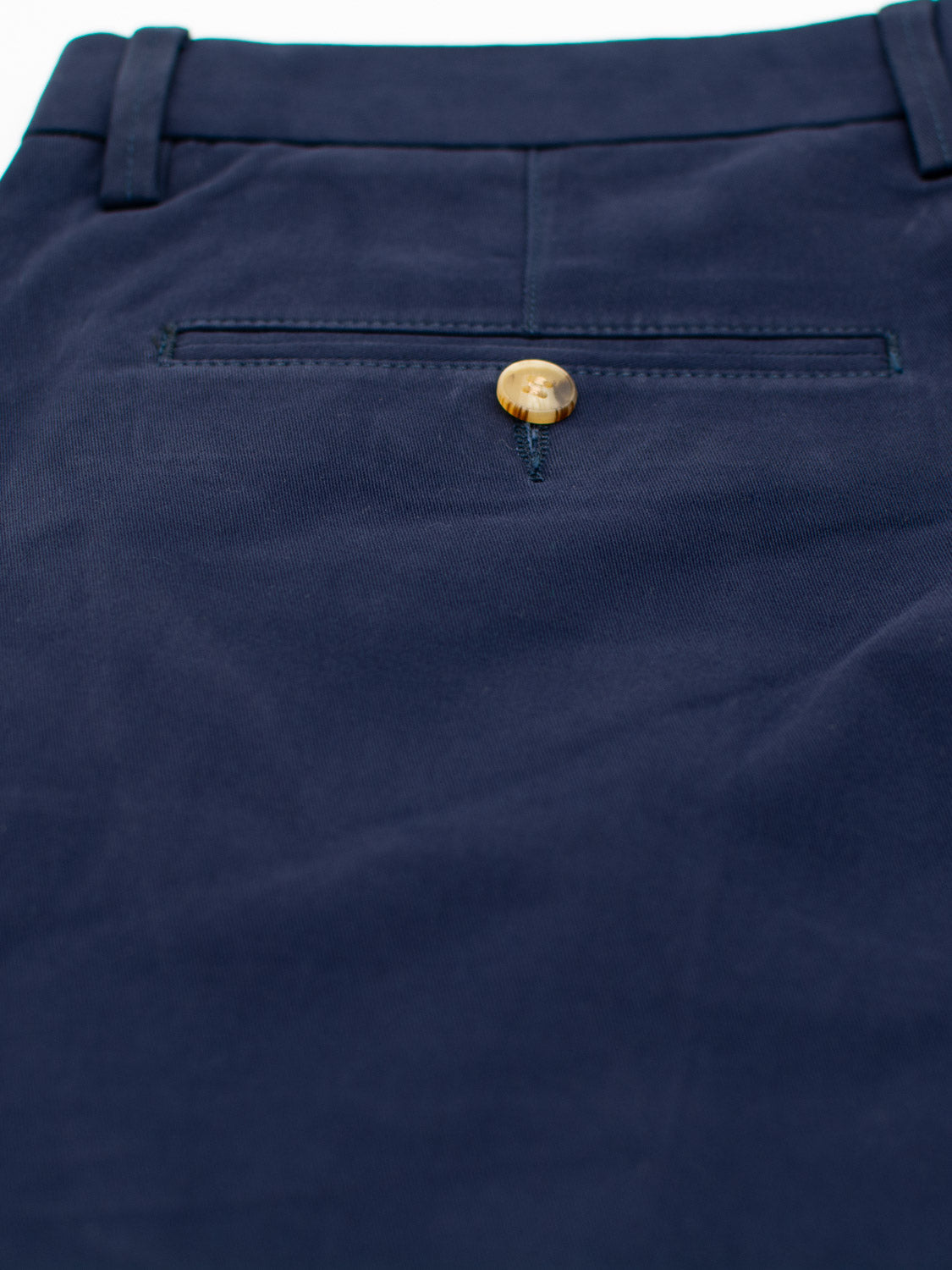 Close-up of navy blue Bushwick Twill Stretch Chino by ID Menswear, showcasing a single back pocket with button closure. The soft cotton twill fabric is slightly wrinkled, with visible belt loops and embodying a relaxed-fit style.