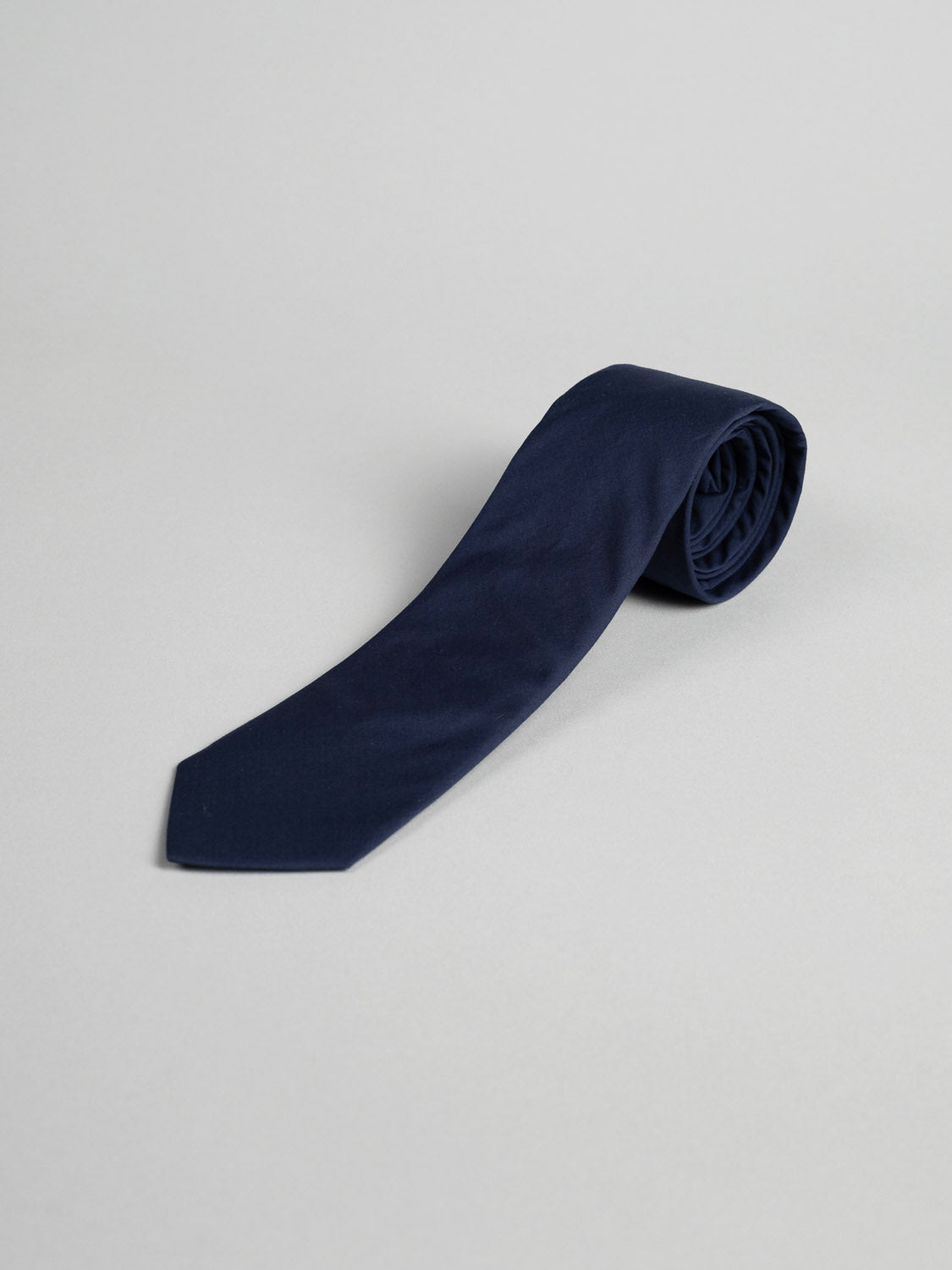 A Liberty of London Tana Lawn™ Navy Tie by ID Menswear, handmade in Brooklyn from premium cotton, is rolled up and placed on a light gray surface.