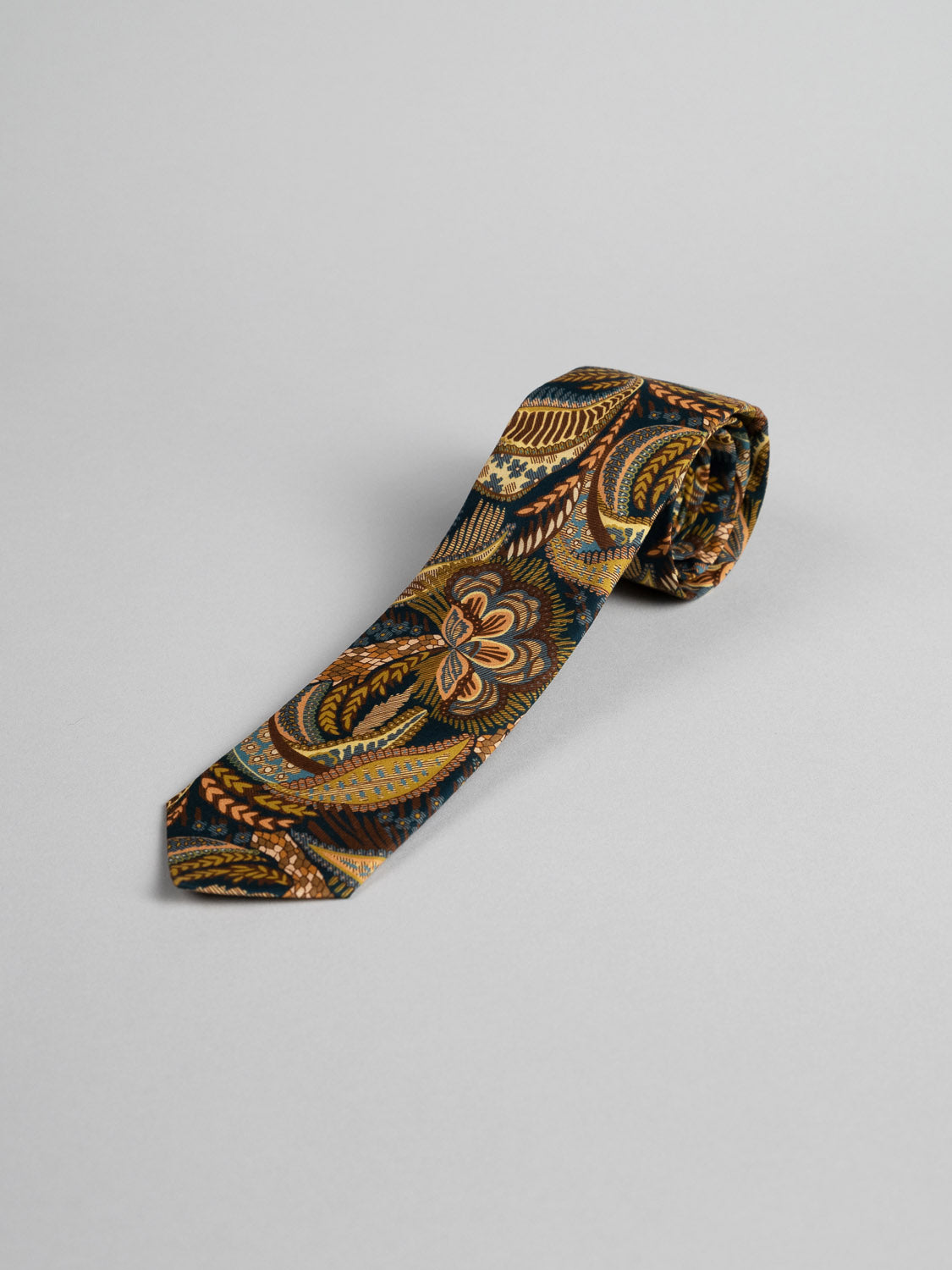 The Liberty of London Tana Lawn™ Medusa Tie by ID Menswear features a gold, brown, and black paisley pattern. Handmade in Brooklyn, its shown rolled on a light gray background.