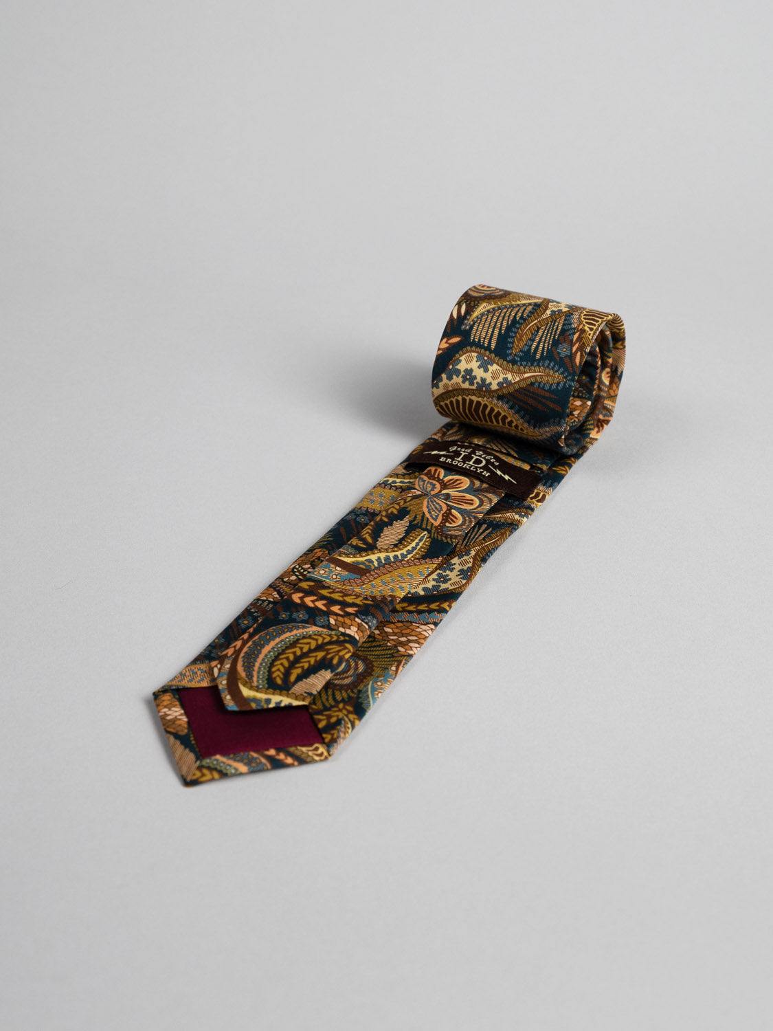 The Liberty of London Tana Lawn™ Medusa Tie by ID Menswear is handmade in Brooklyn from Tana Lawn cotton, featuring a vibrant paisley and floral pattern in gold, green, blue, and red on a light gray background.