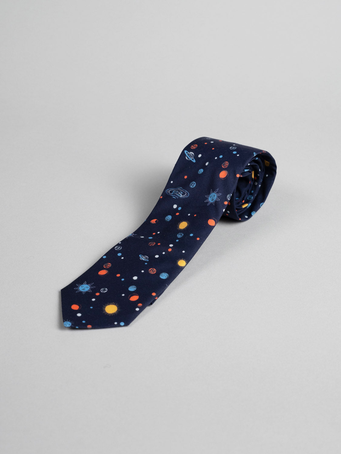 The Liberty of London Tana Lawn™ Niko Tie by ID Menswear is handmade in Brooklyn from soft cotton, featuring a colorful space-themed pattern with planets, stars, and rockets on a light gray background.