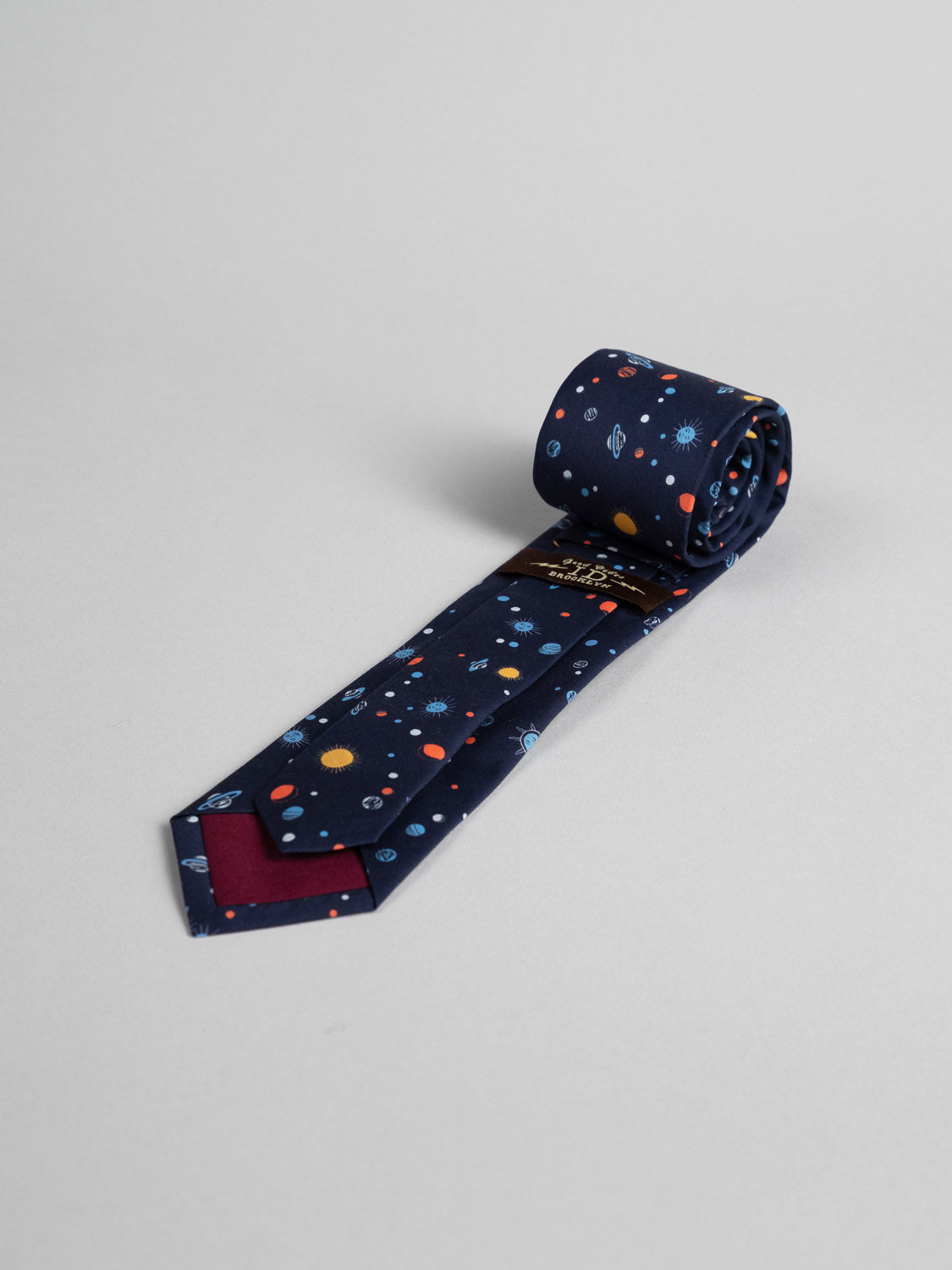 The Liberty of London Tana Lawn™ Niko Tie by ID Menswear is handmade in Brooklyn from soft cotton, featuring a vibrant space-themed pattern with planets and stars on a light gray background.