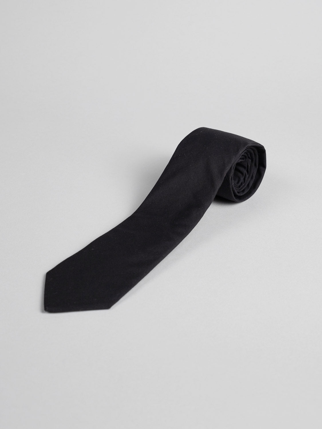 The Liberty of London Tana Lawn™ Noir Tie by ID Menswear, made from luxurious black Tana Lawn cotton with a pointed tip, is neatly rolled and displayed on a plain light gray background.