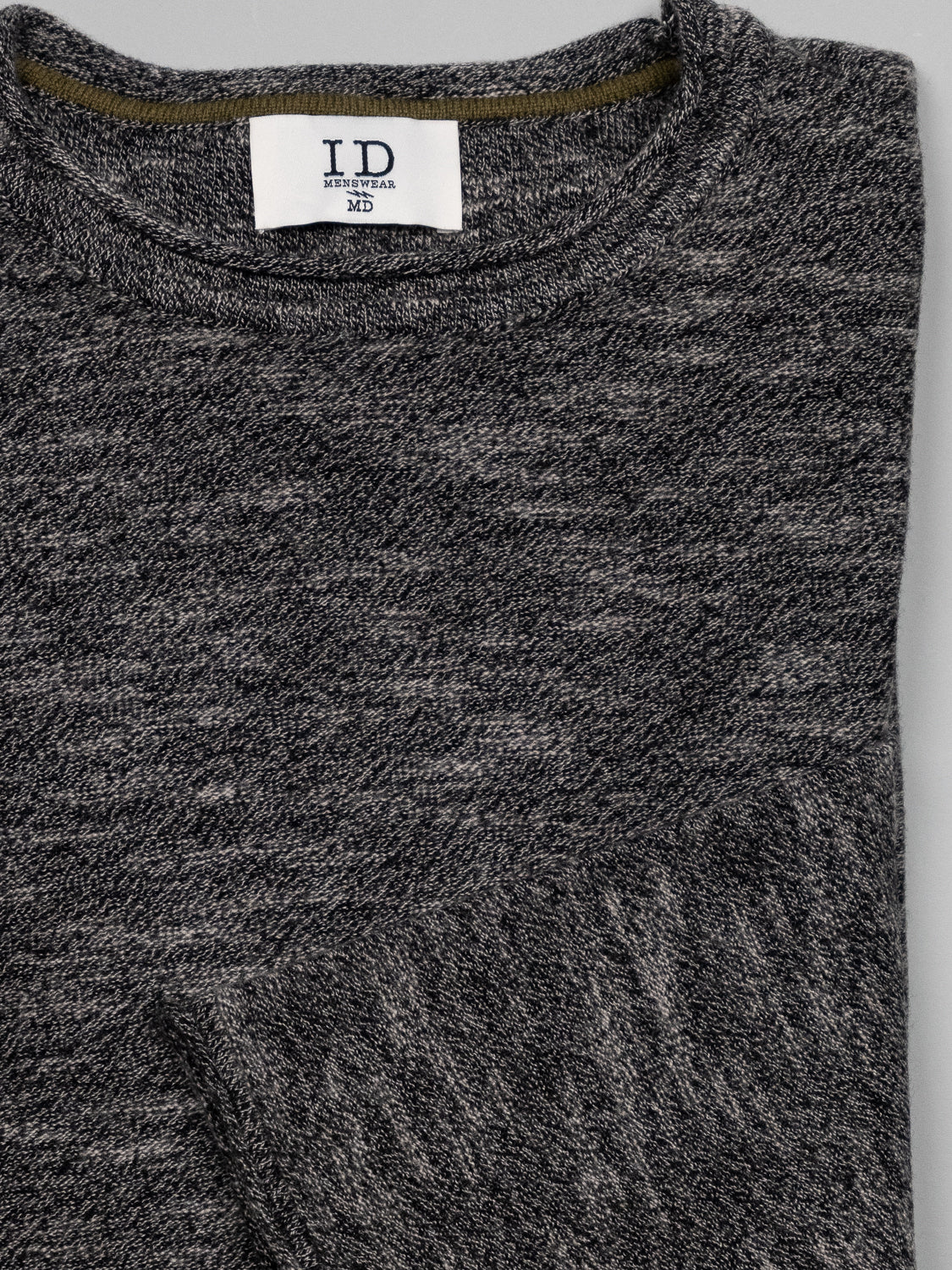 Close-up of a folded Maverick Rolled Neck Sweater by ID Menswear in gray Merino wool with a marled texture. The fabric looks soft and cozy, offering lightweight warmth. A collar label is visible, but the text is not discernible. The image highlights the fabric and sophisticated detailing.