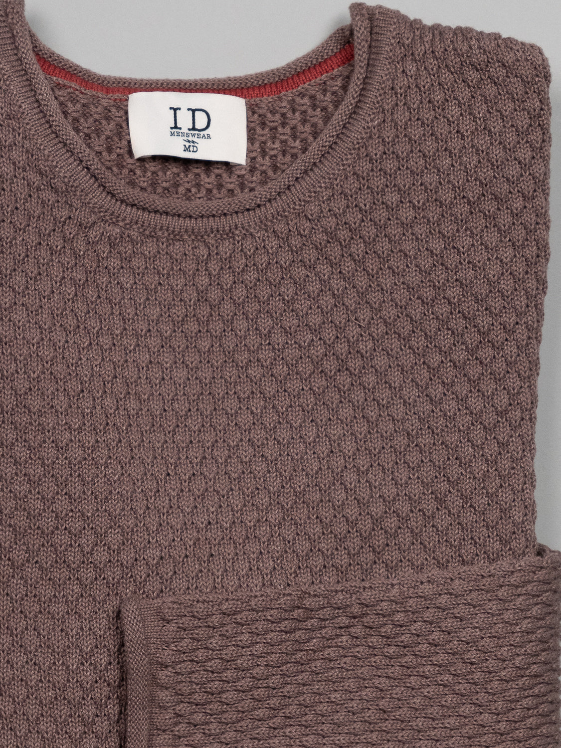 The Westside Rolled Neck Sweater by ID Menswear is a brown textured knitwear featuring a pineapple needle pattern and waffle-knit design, with a subtle red trim inside the collars edge. It comes neatly folded with an ID label, size M.
